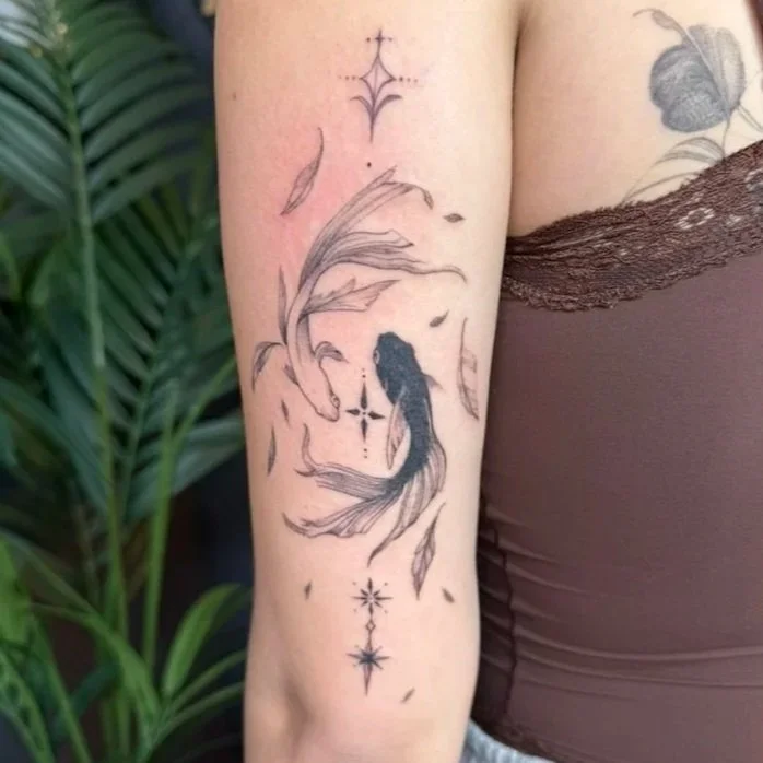 Tattoo of a koi fish with flowing fins surrounded by decorative elements on person's upper arm.
