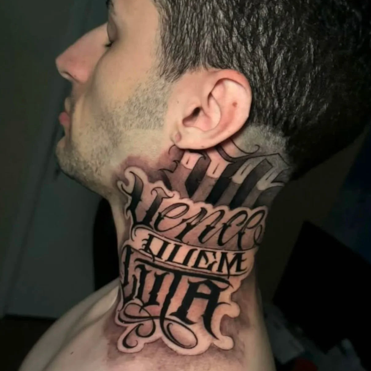 Close-up of a man's neck tattoo with elaborate black script lettering.