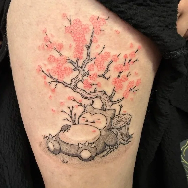 A tattoo of a cute, round creature resembling a mix between a bear and a Pokémon, resting against a tree stump with a large cherry blossom tree growing behind it, with pink flowers and petals.