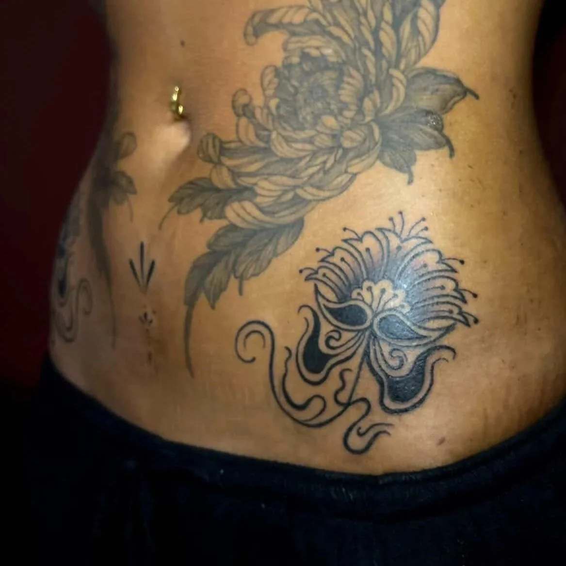 Tattoo on a person's lower abdomen featuring a tiger lily flower and an intricate, stylized skull with floral designs.