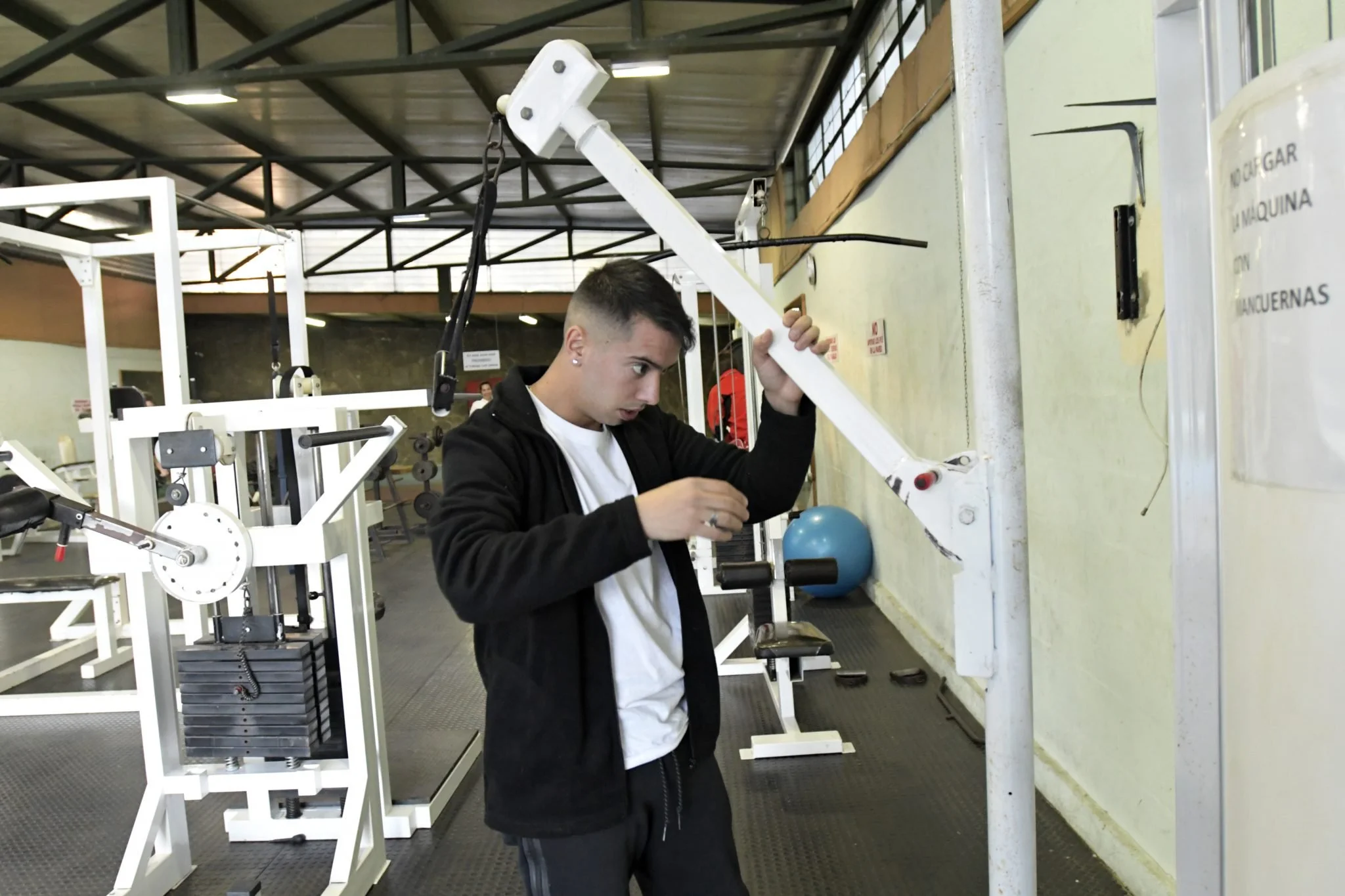 A young man standing in a gym adjusting a piece of workout equipment.