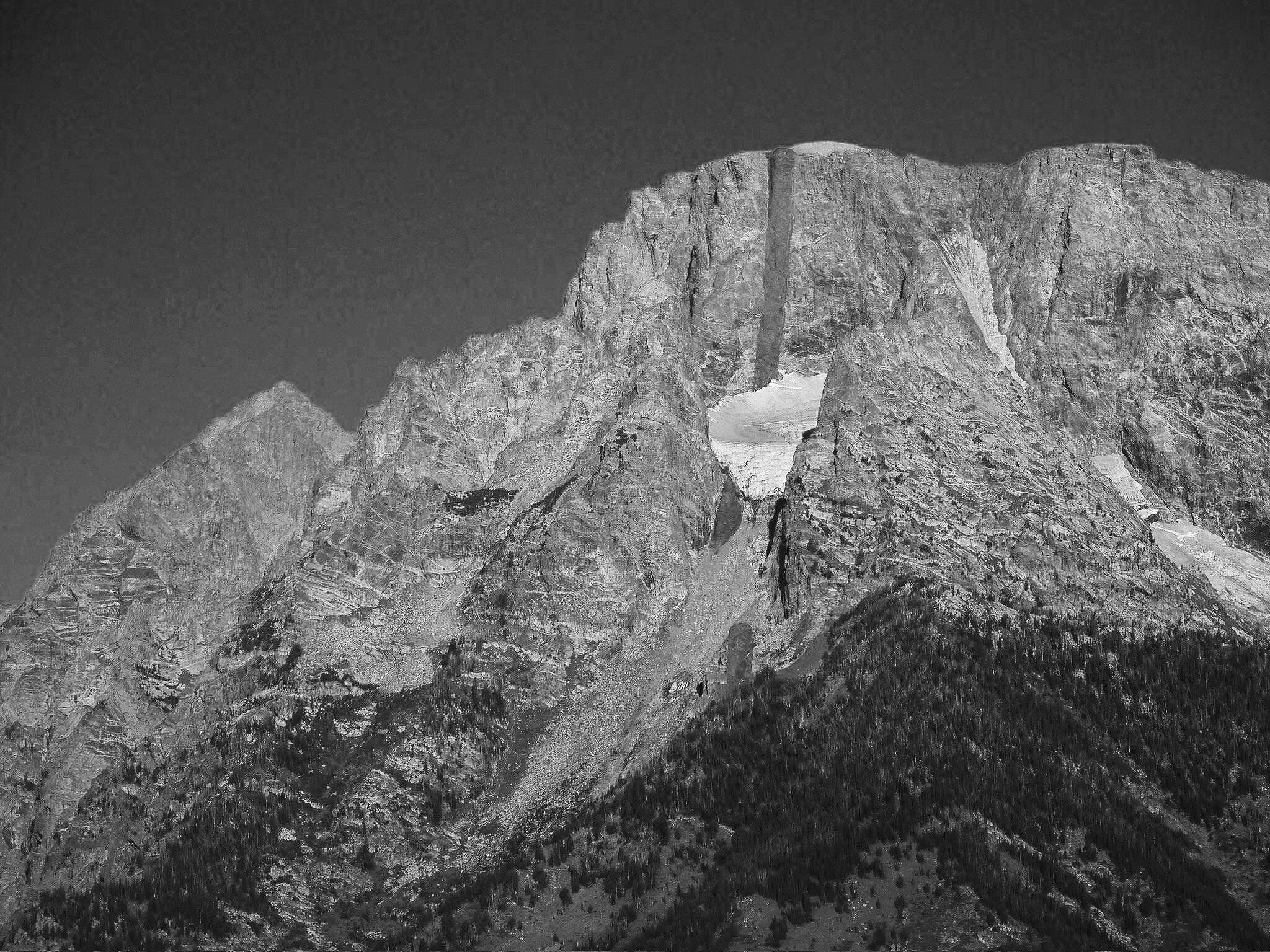 Black and white photograph of a large mountain with a natural arch formation, steep rocky slopes, and a forested lower section.