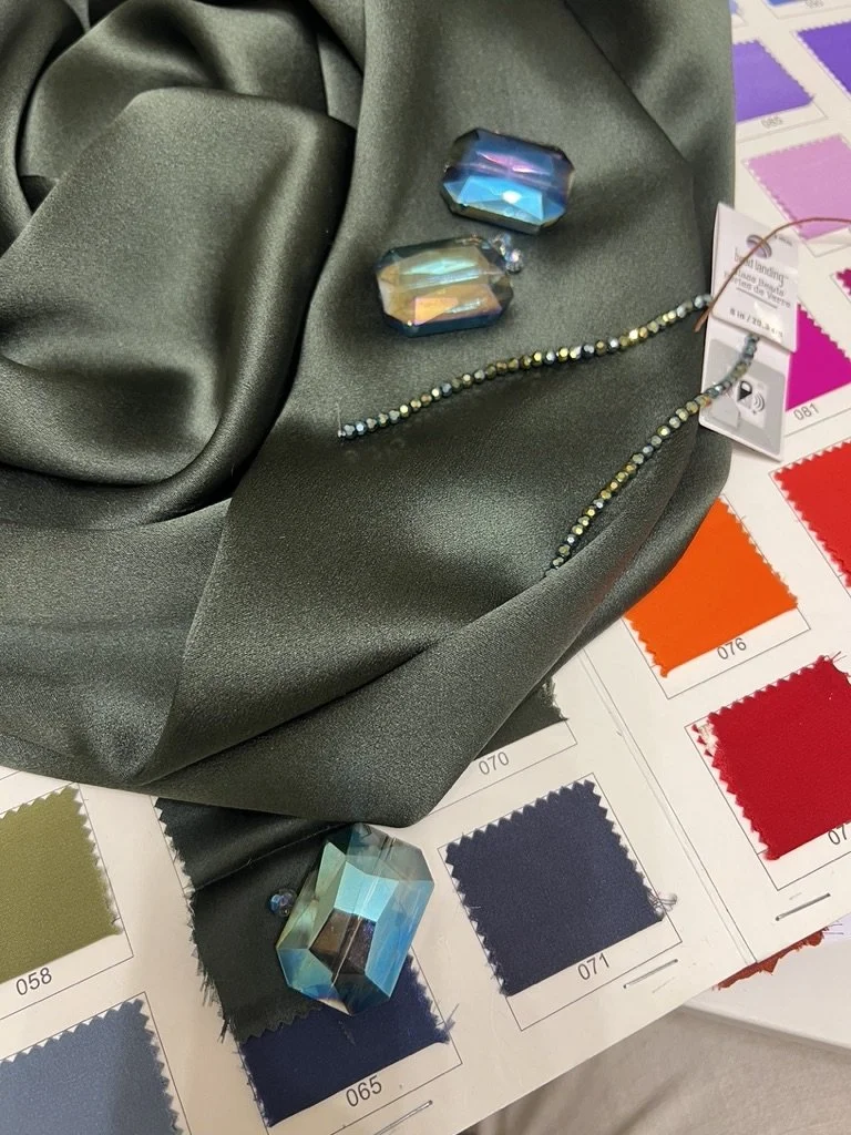 Dark green silk charmeuse and color swatches with beading samples at Angeline Brunk's private design studio where she guides her luxury clients through fit, fabric, and style options for their upcoming weddings and special occasions in Seattle.
