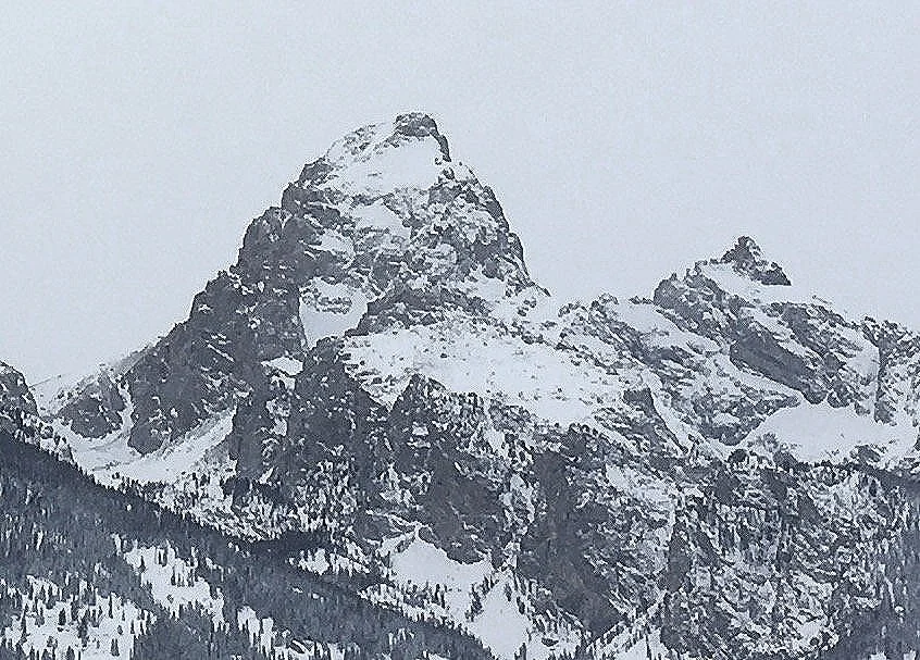 Snow-covered Grand Teton mountain peak in Jackson Hole, Wyoming with rugged rocky surface and forested slopes.
