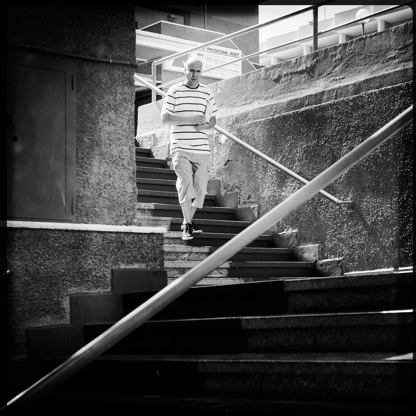 A man walking down exterior staircase with textured walls and metal handrails in black and white photo.
