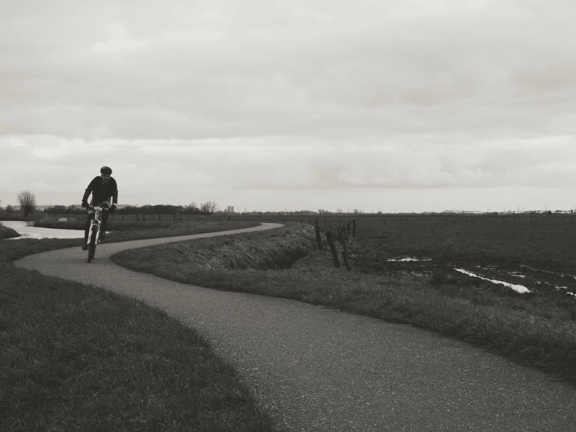 A person riding a bicycle along a winding path in a rural area under cloudy skies.