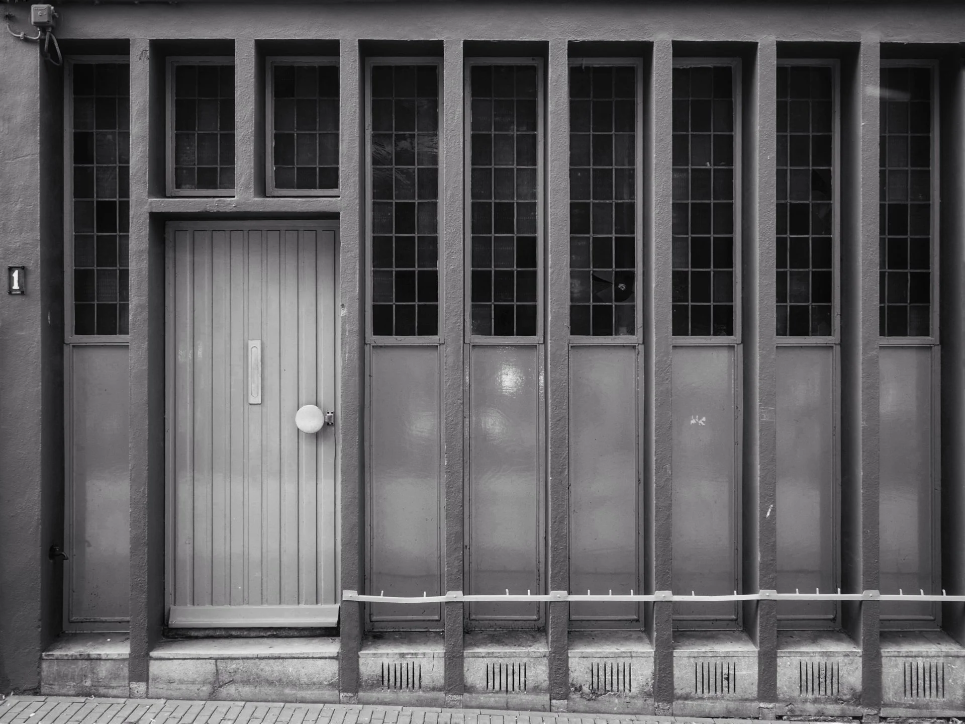 Black and white photo of a garage door with small windows at the top and a white vertical door with a round handle, with a security chain in front.