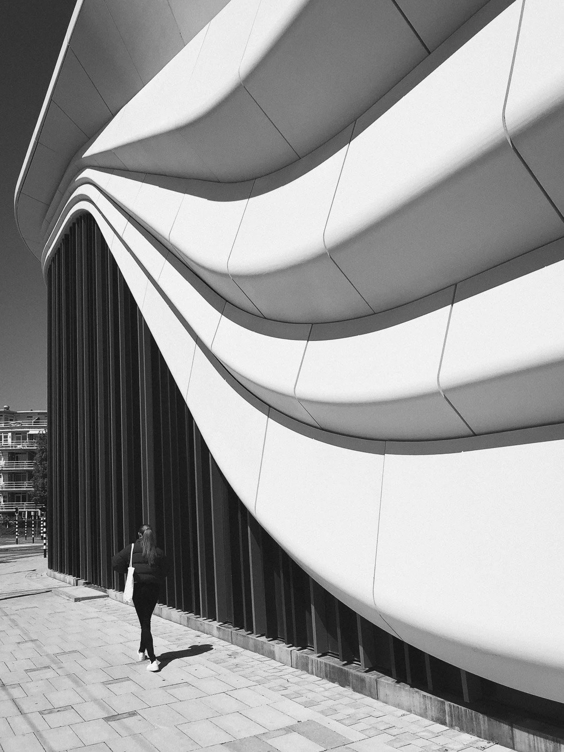 A woman walking past a modern building with curved, layered architectural design in black and white.