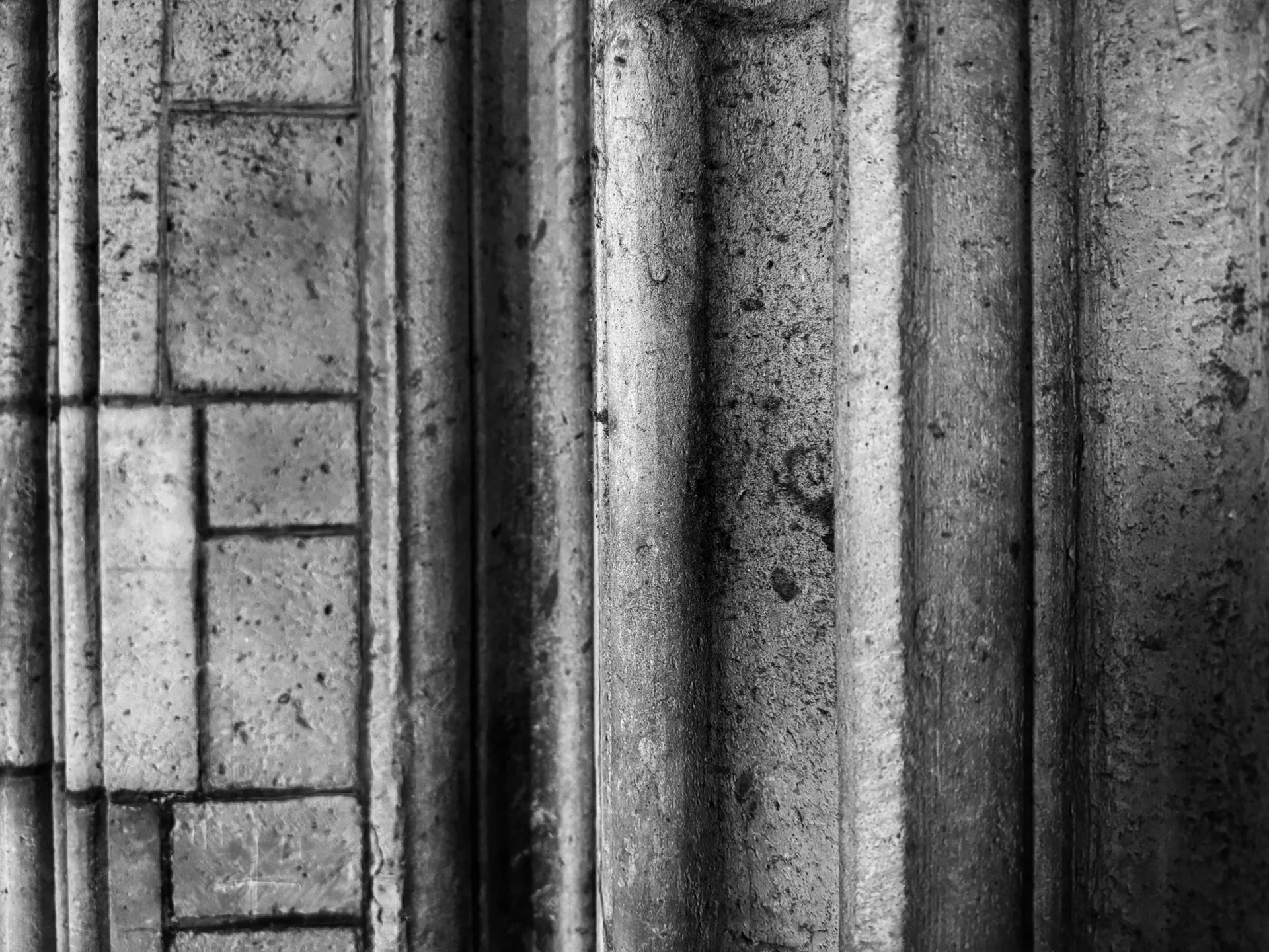 Een close-up zwart-wit foto van een muur met bakstenen en betonblokken, verticale lijnen en texturen.