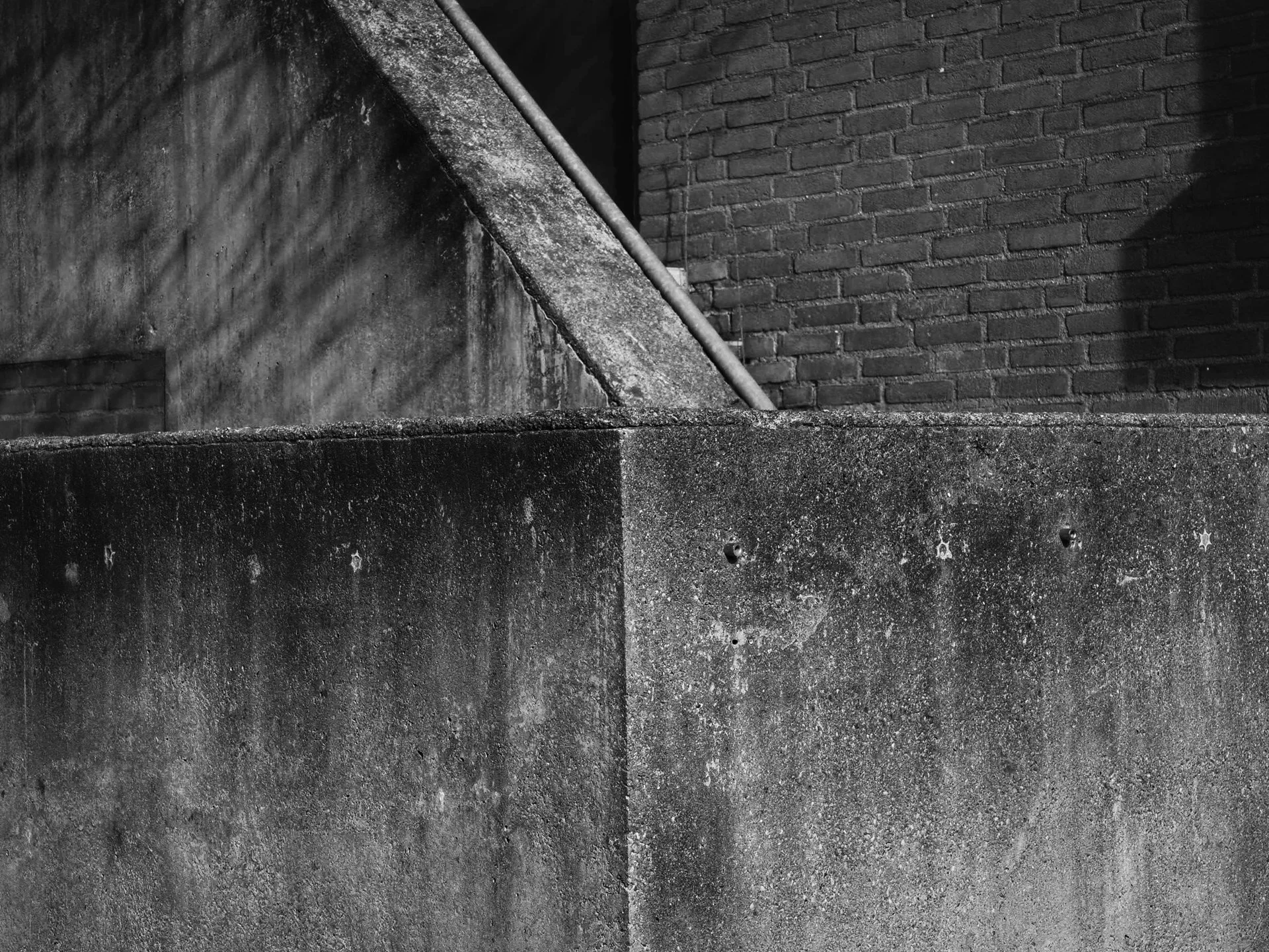 Black and white photo of concrete structure with stairs and brick wall in the background.