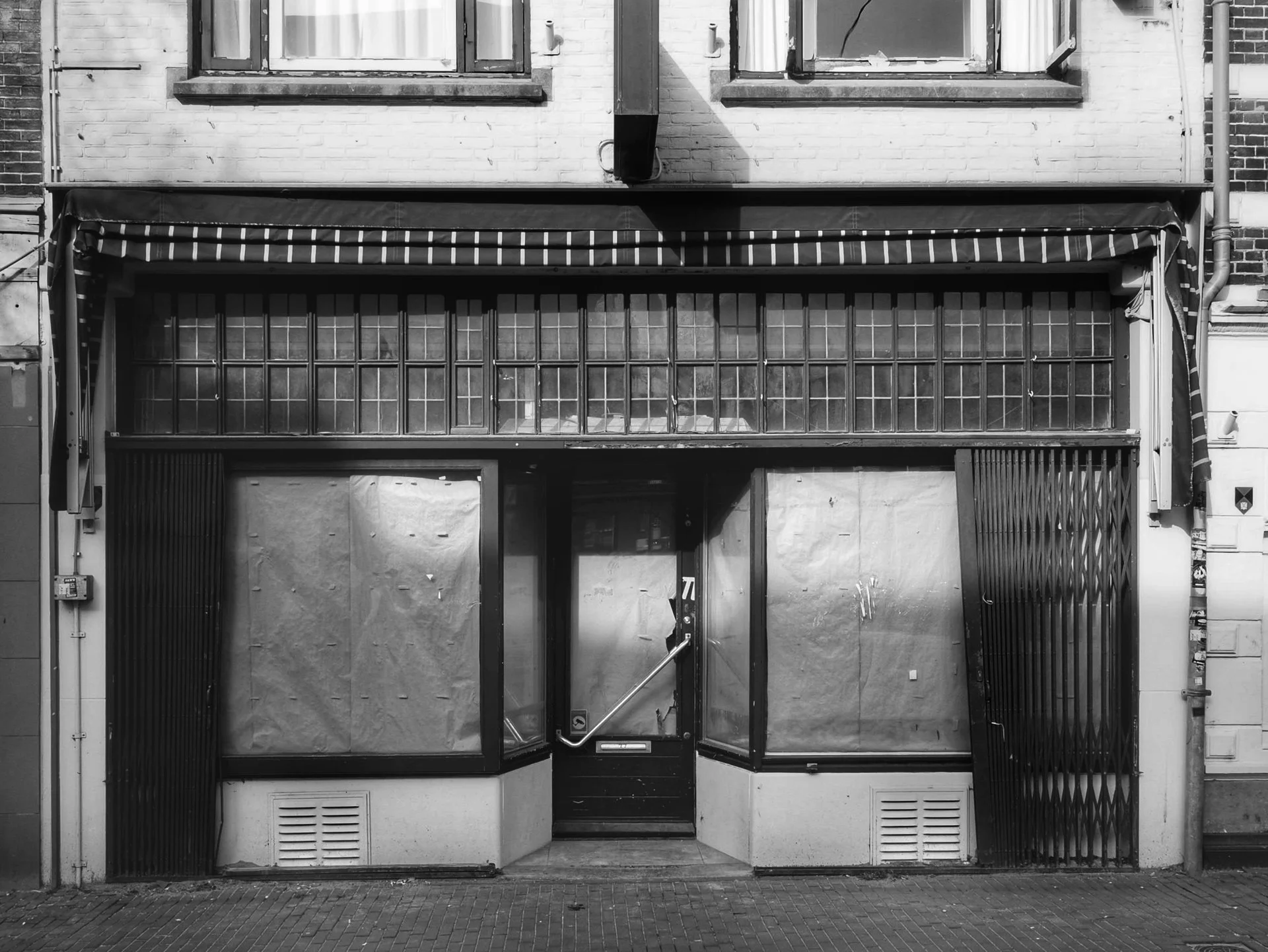 Black and white photo of a closed storefront with boarded-up windows and a central glass door.