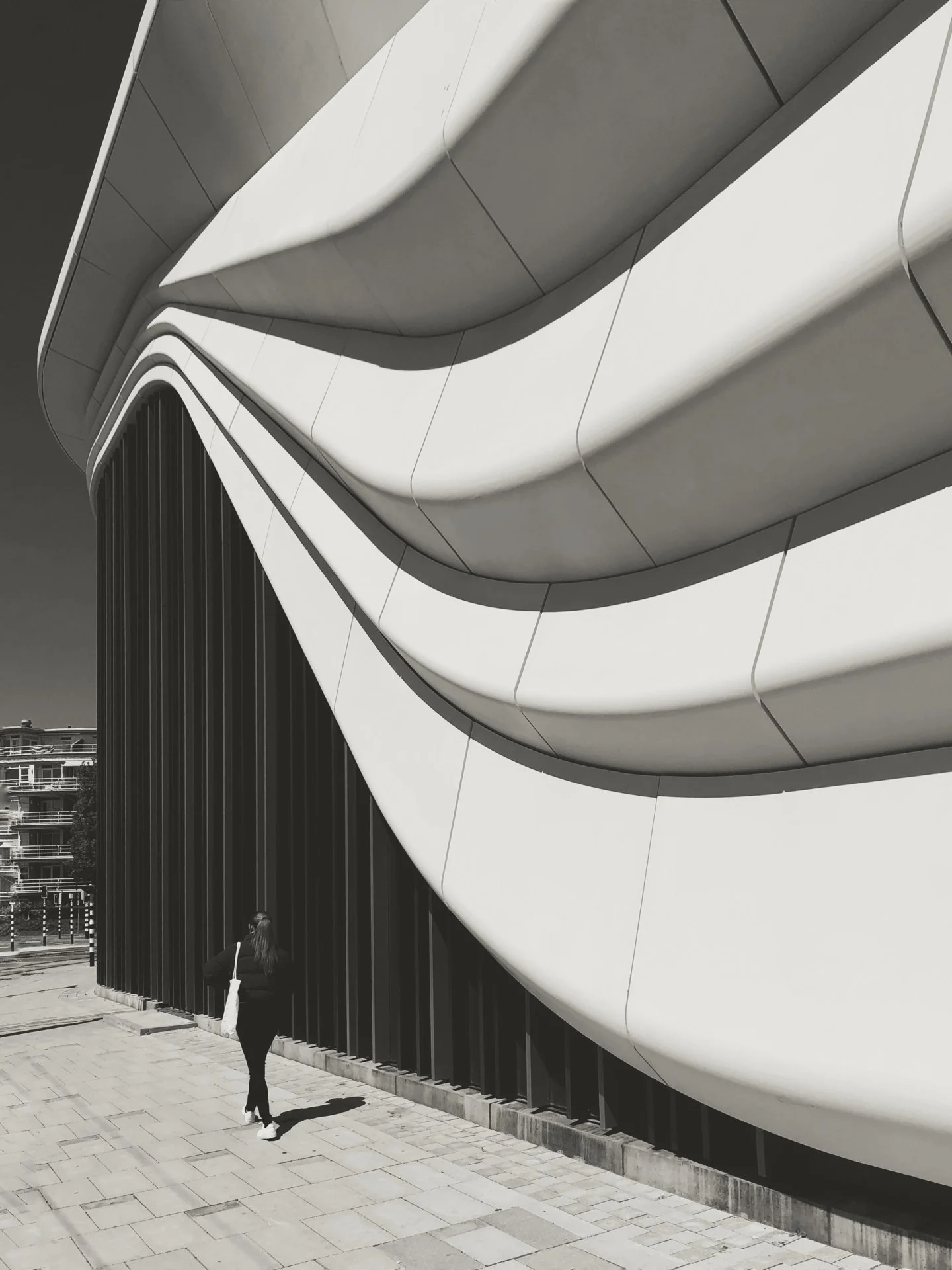 A person with long hair walking beside a modern building with curved white and black architectural elements.
