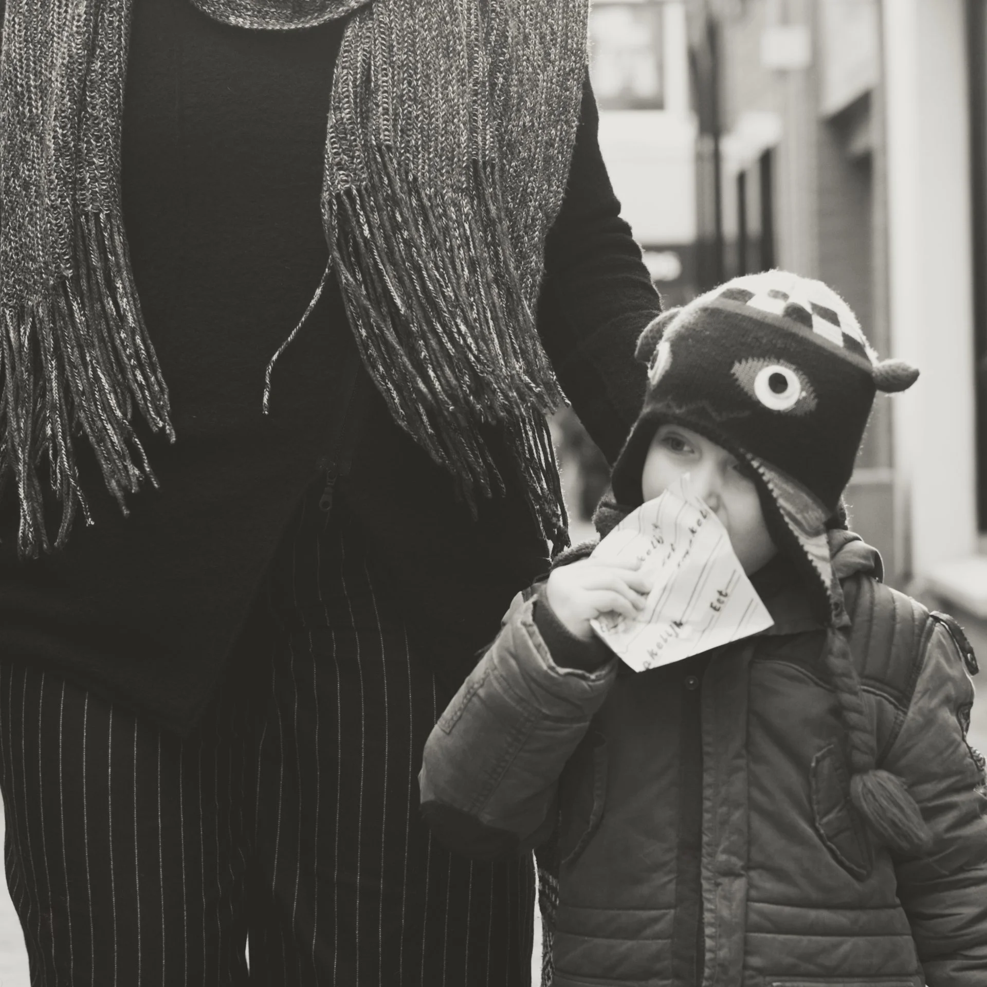 A person wearing a striped skirt and a textured scarf standing next to a child in a winter jacket and hat, holding a paper.