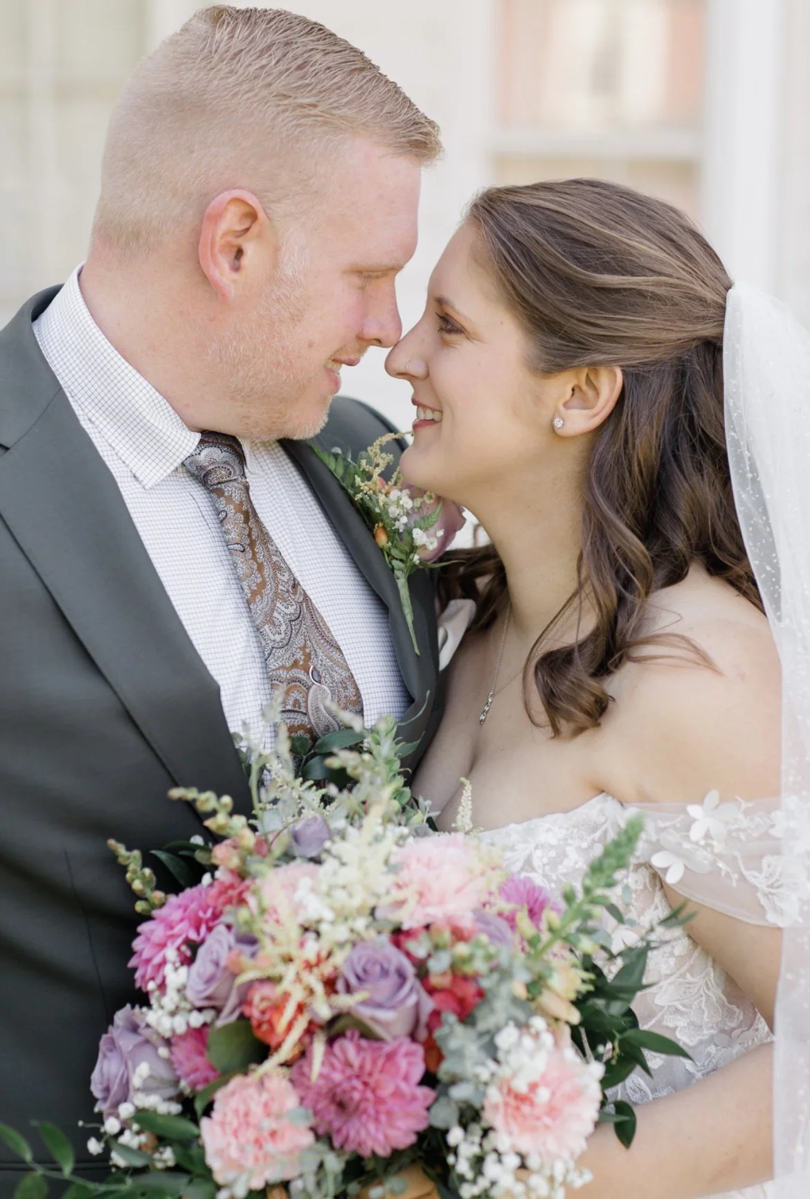 Bride and groom embracing, holding a colorful bouquet with pink and purple flowers.