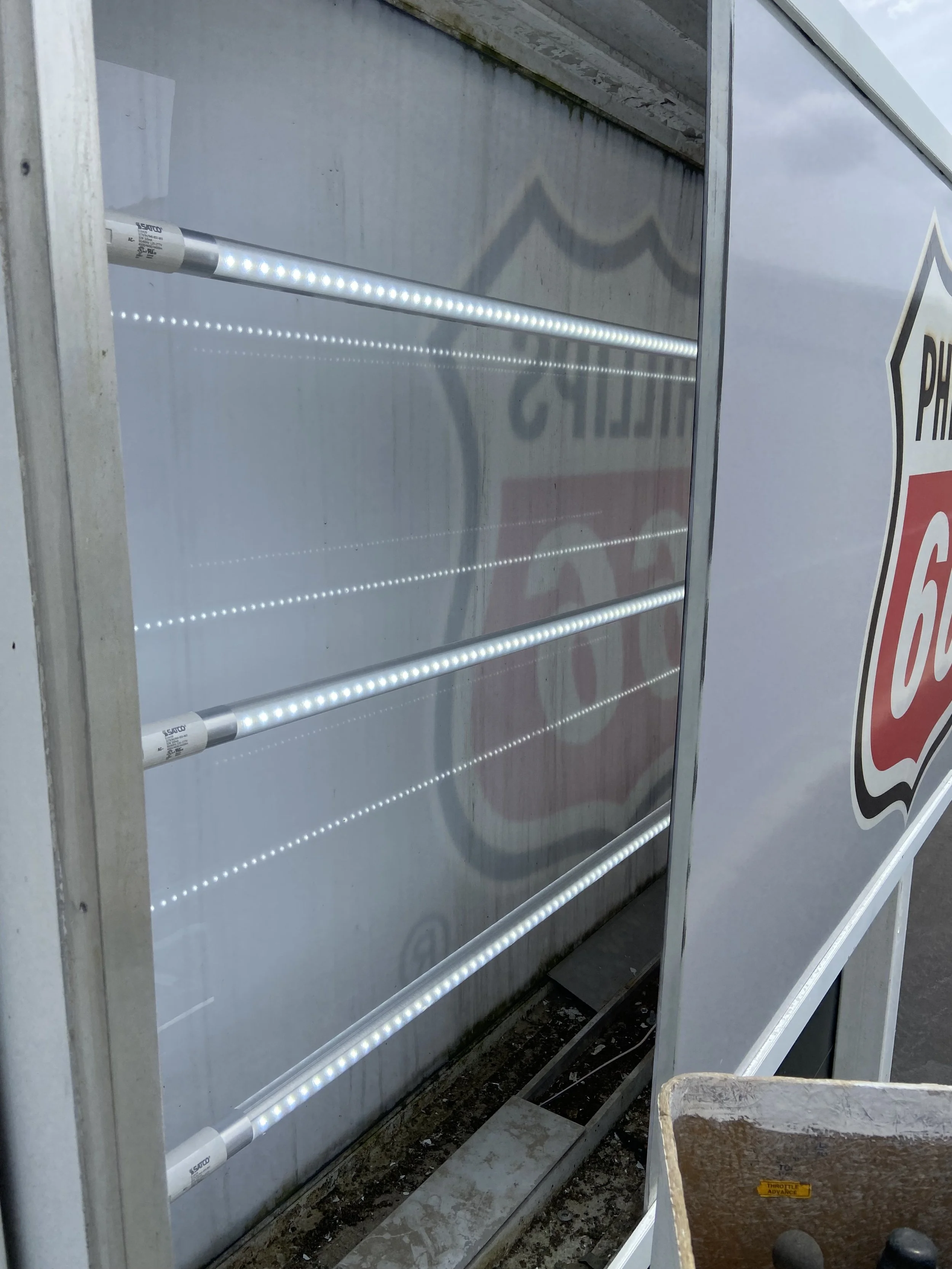 The image shows a partially disassembled vending machine with visible LED lighting strips and a sign behind it reflecting on the glass.