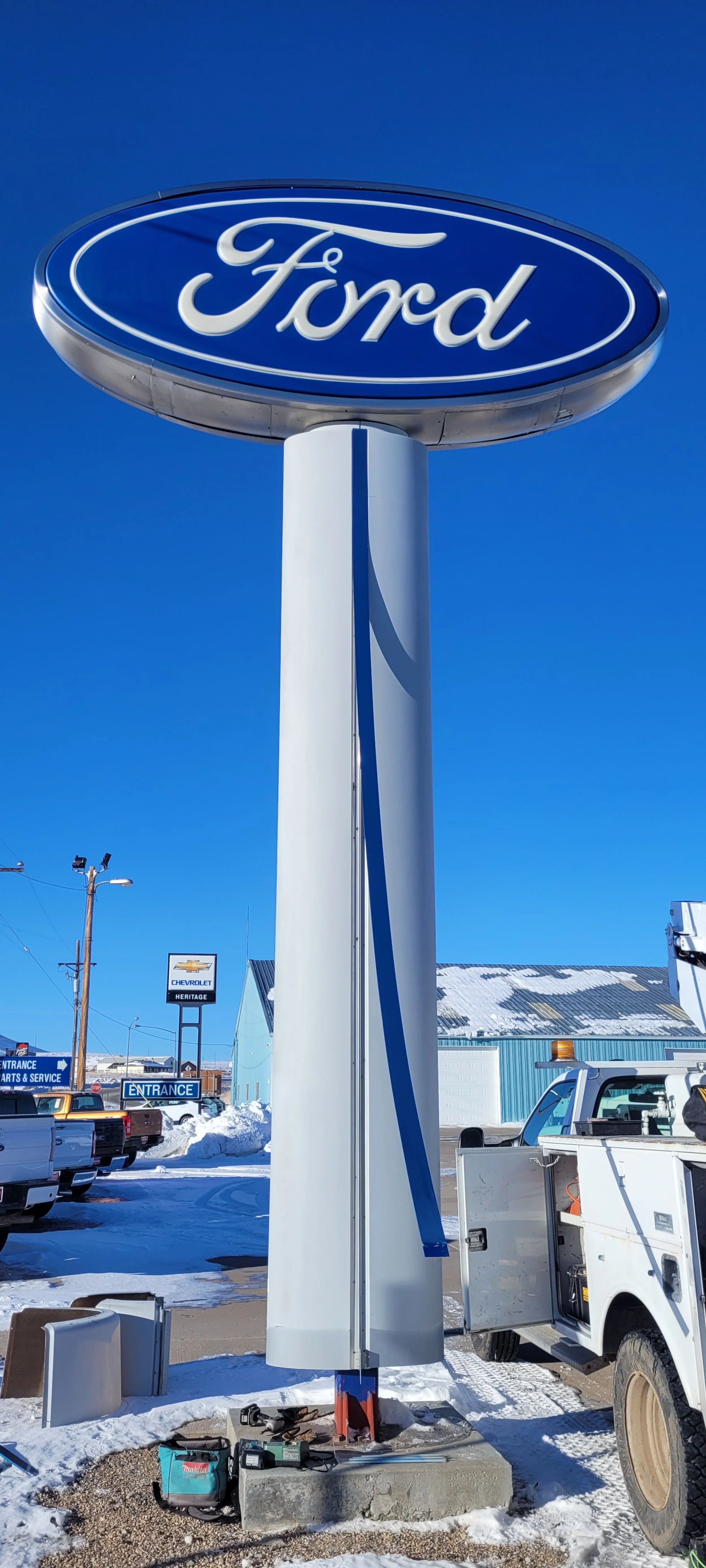 Large illuminated Ford sign being installed outdoors on a snowy day, with work tools and a utility vehicle nearby.