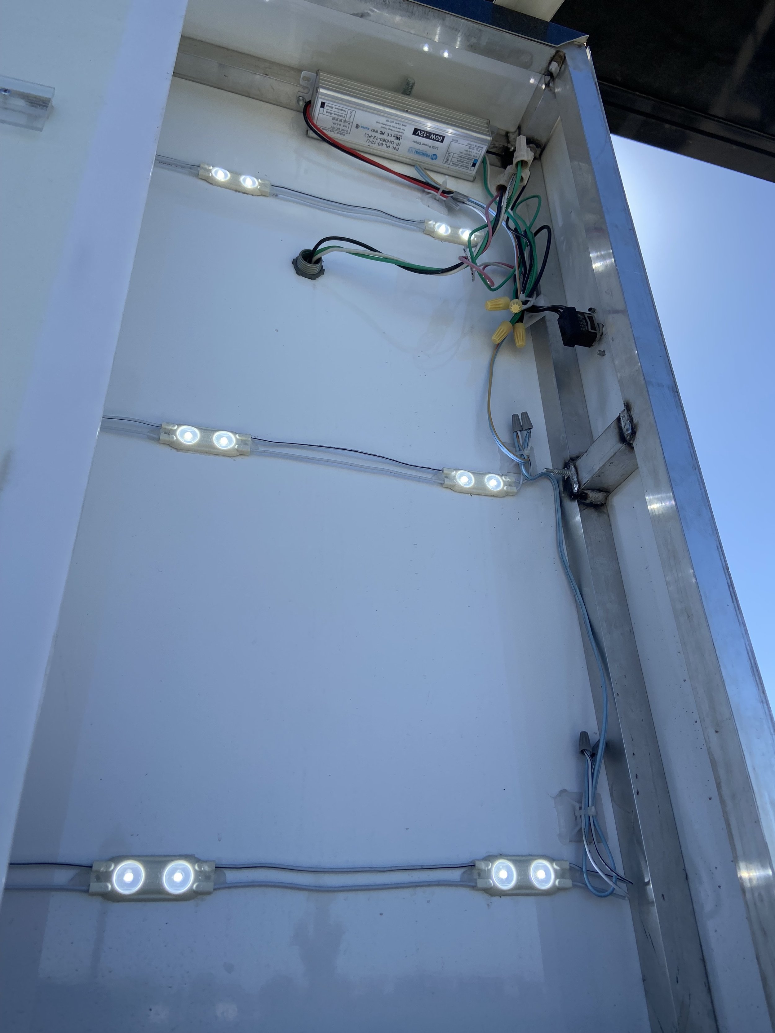 Interior of an electrical enclosure with a power supply, wiring, and LED lights installed along the walls.