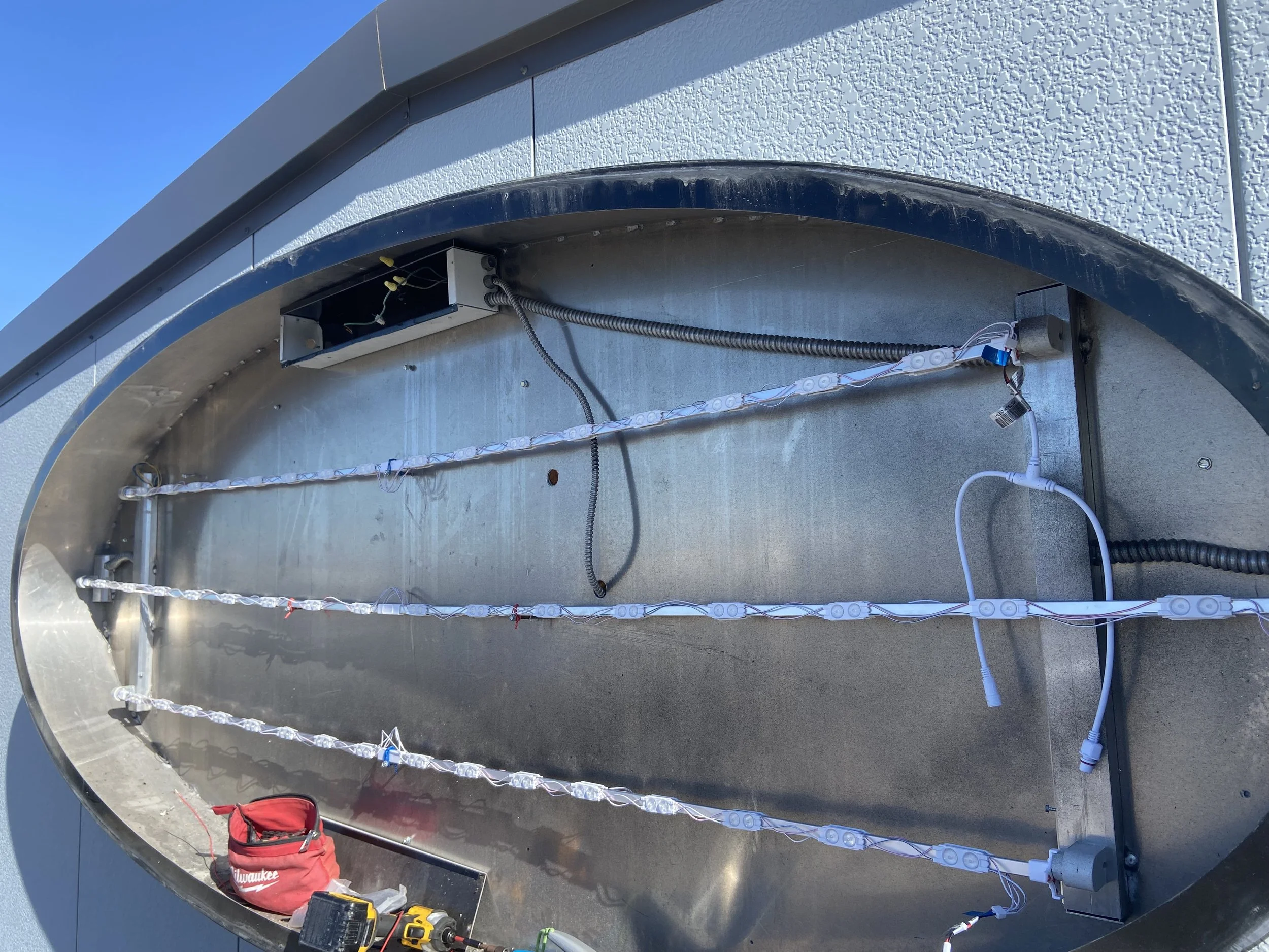 Installation of LED strip lights inside a metal outdoor structure with wiring and tools visible.
