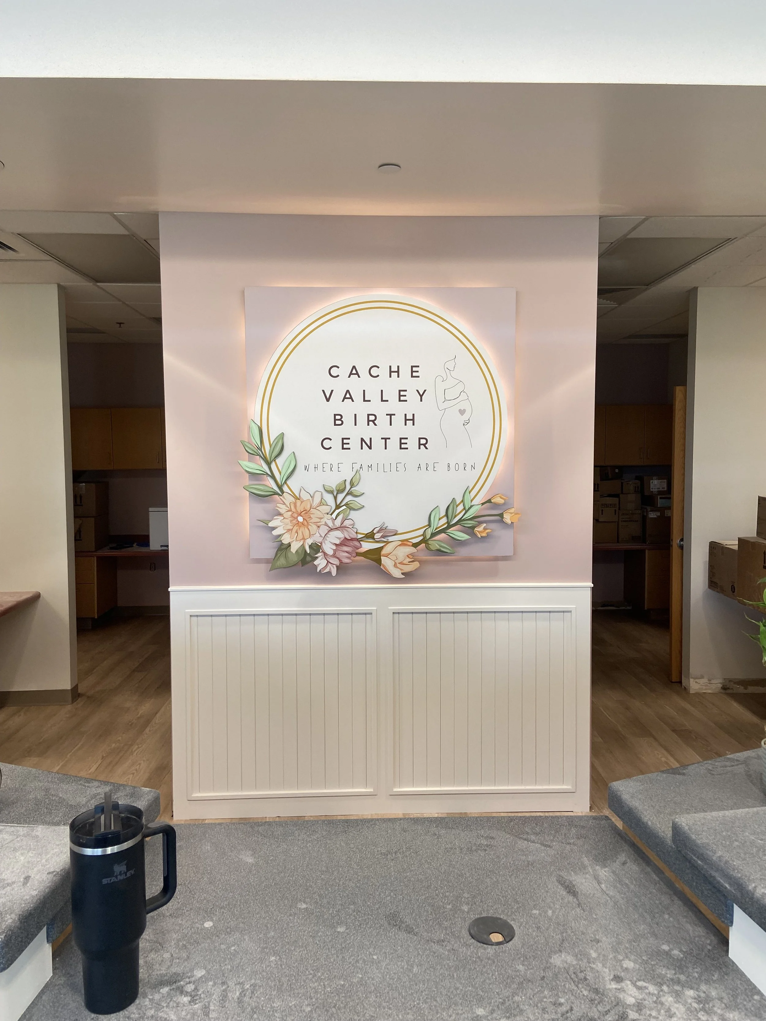 A sign for Cache Valley Birth Center with floral decorations and the tagline 'Where families are born' inside a building.