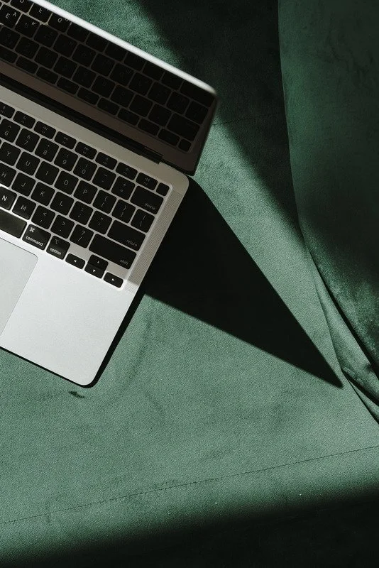 Close-up of a silver laptop with black keyboard resting on a green fabric surface, with shadows cast on the fabric.