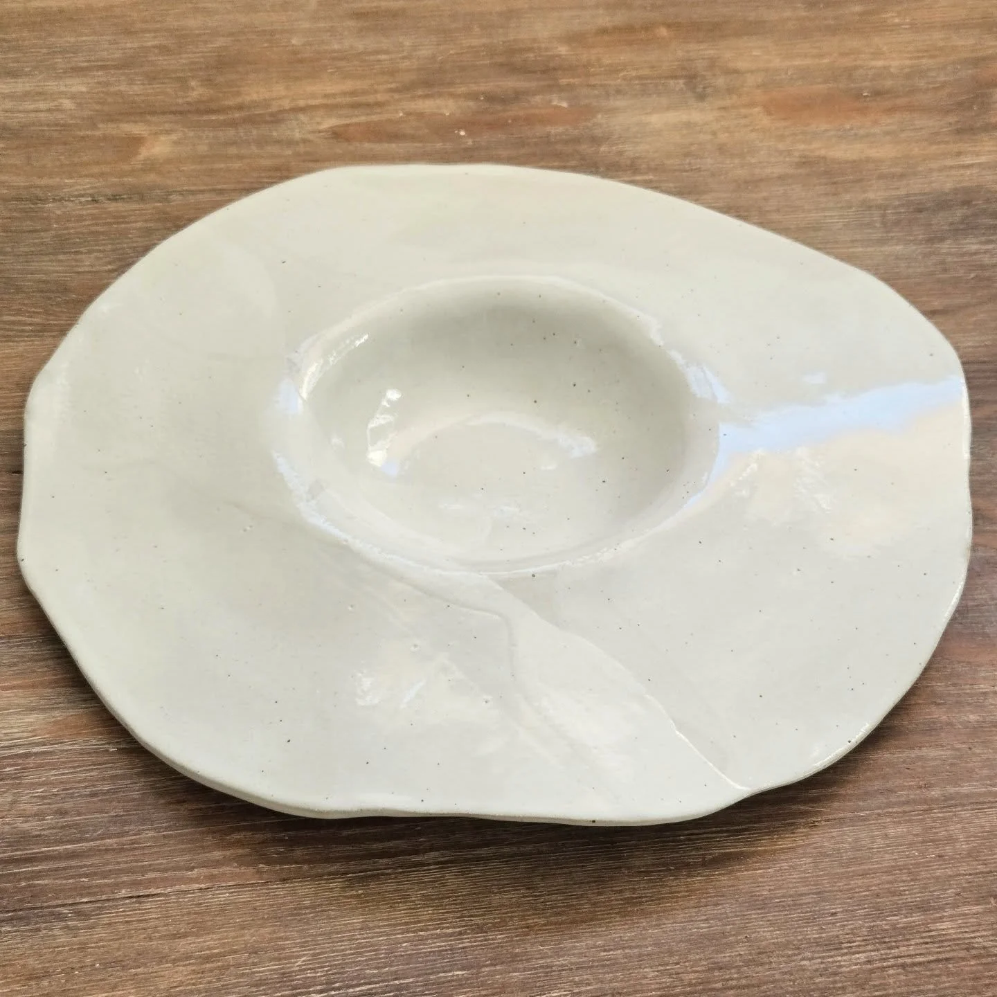 Assiette fa&ccedil;onn&eacute;e en gr&egrave;s, avec une forme libre et dansante. L&rsquo;&eacute;mail "blanc cireux" que je formule laisse appara&icirc;tre, en cuisson de r&eacute;duction, les pointes de fer contenues dans la terre. Ces fi