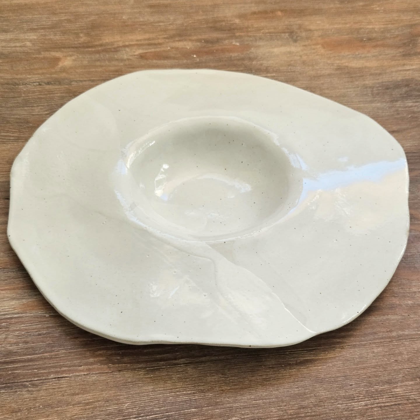 Assiette fa&ccedil;onn&eacute;e en gr&egrave;s, avec une forme libre et dansante. L&rsquo;&eacute;mail "blanc cireux" que je formule laisse appara&icirc;tre, en cuisson de r&eacute;duction, les pointes de fer contenues dans la terre. Ces fi