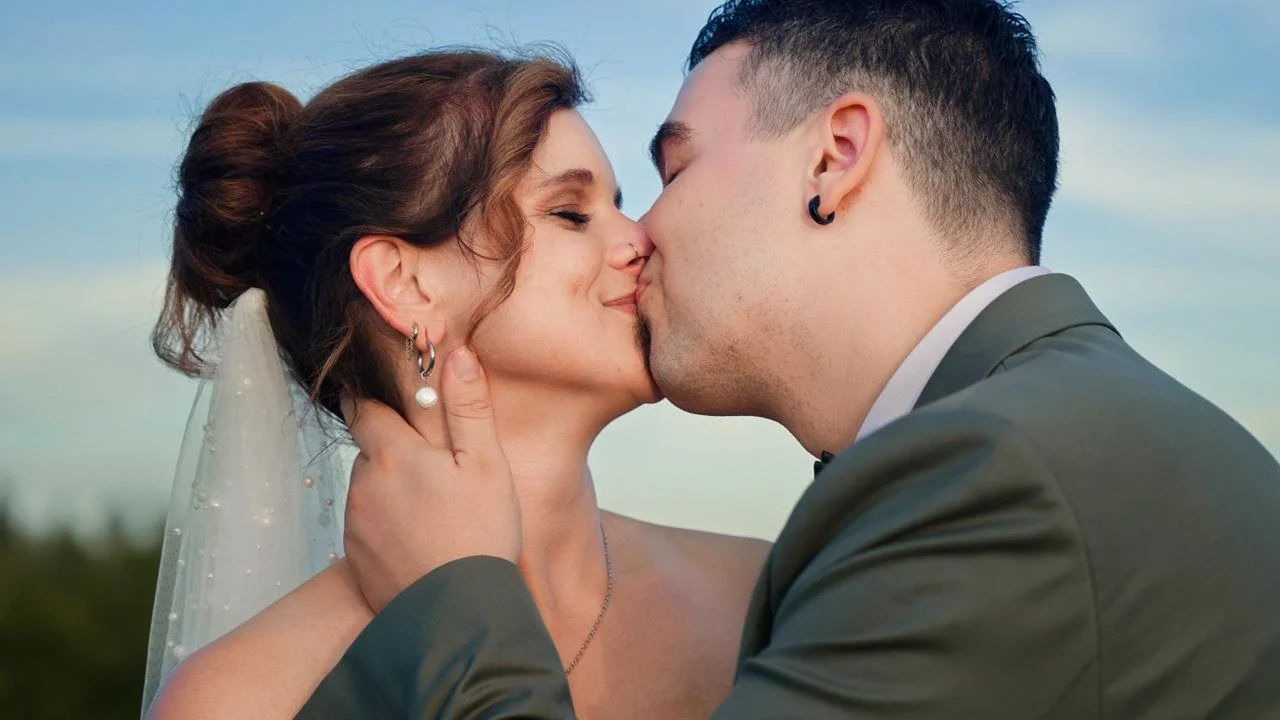 Ein Brautpaar küsst sich bei Sonnenuntergang, die Frau trägt eine Hochzeitstorte und die Männer tragen einen Anzug.