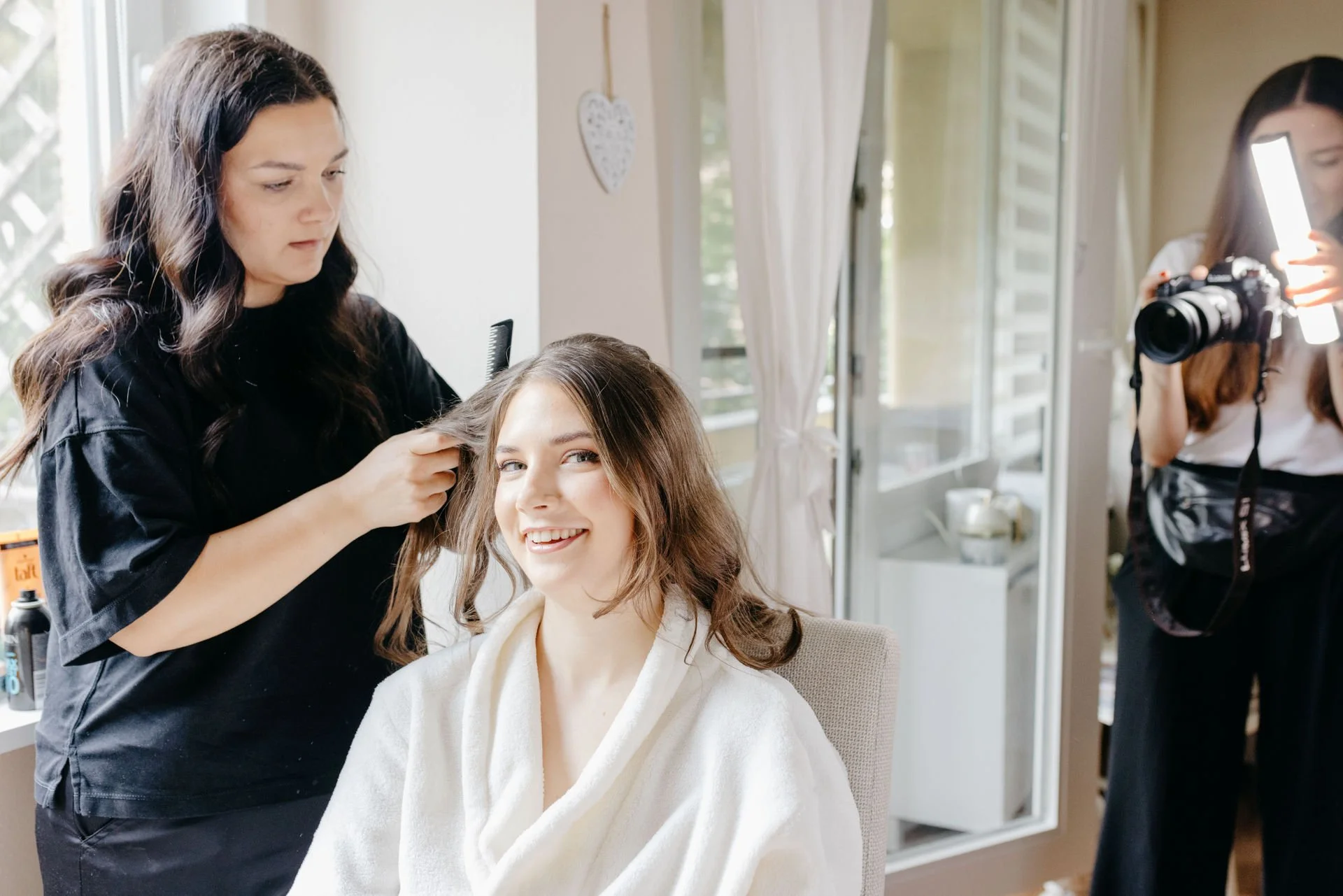 Braurstylistin macht einer Braut die Haare, während die Videografin Sofia von der LoCrew ihr Getting Ready filmt.