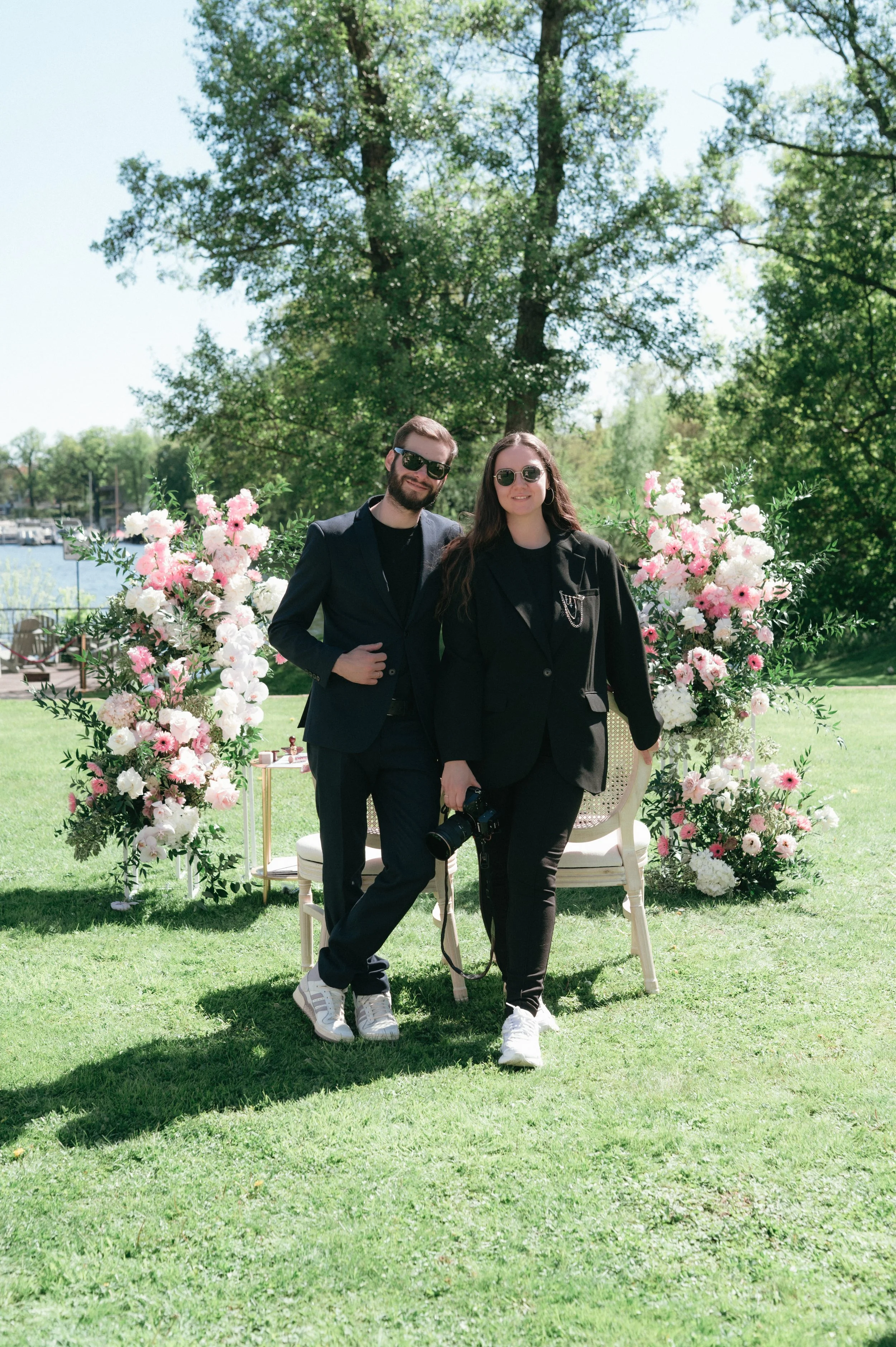 Nico und Sofia LoCrew stehen vor einer Blumeninstallation im Freien an einem sonnigen Tag.