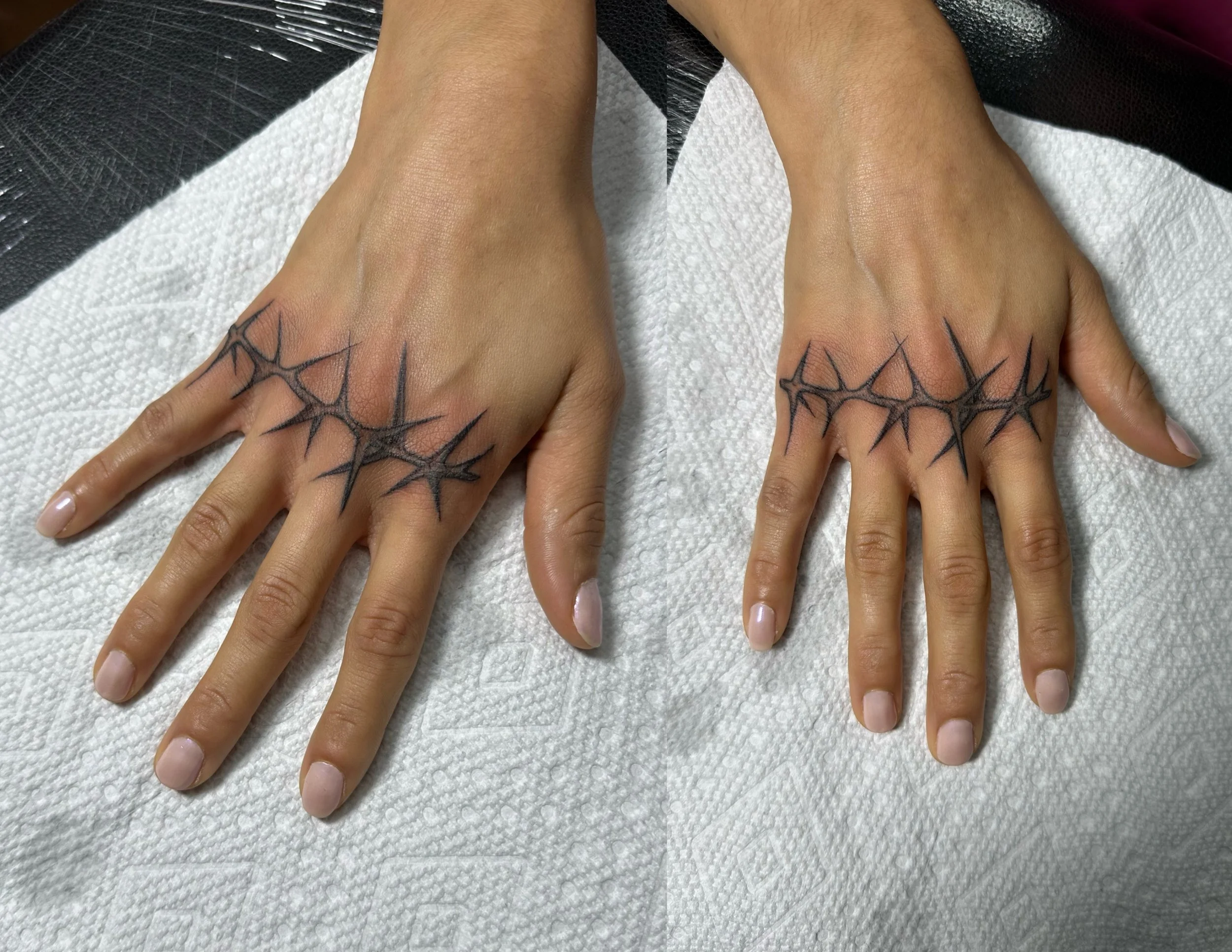 A pair of hands with black spider web tattoos on the wrist and lower fingers, resting on a white surface with a textured pattern, next to a black leather object.
