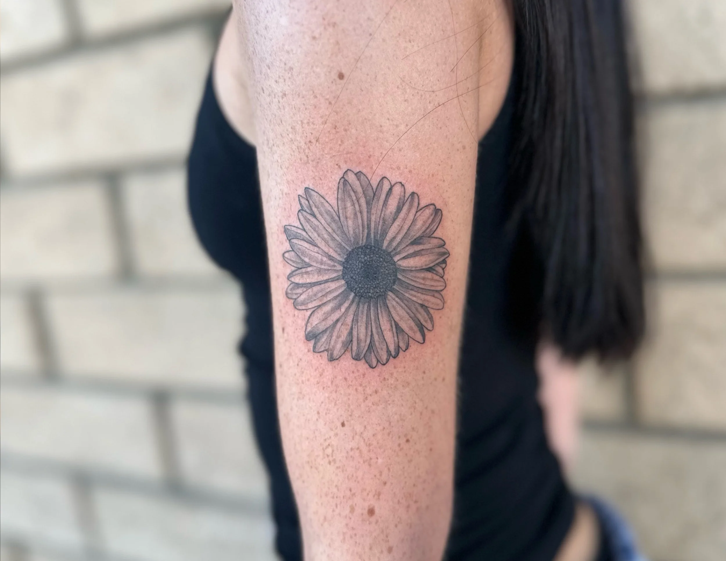 Close-up of a person's upper arm with a black and white sunflower tattoo.