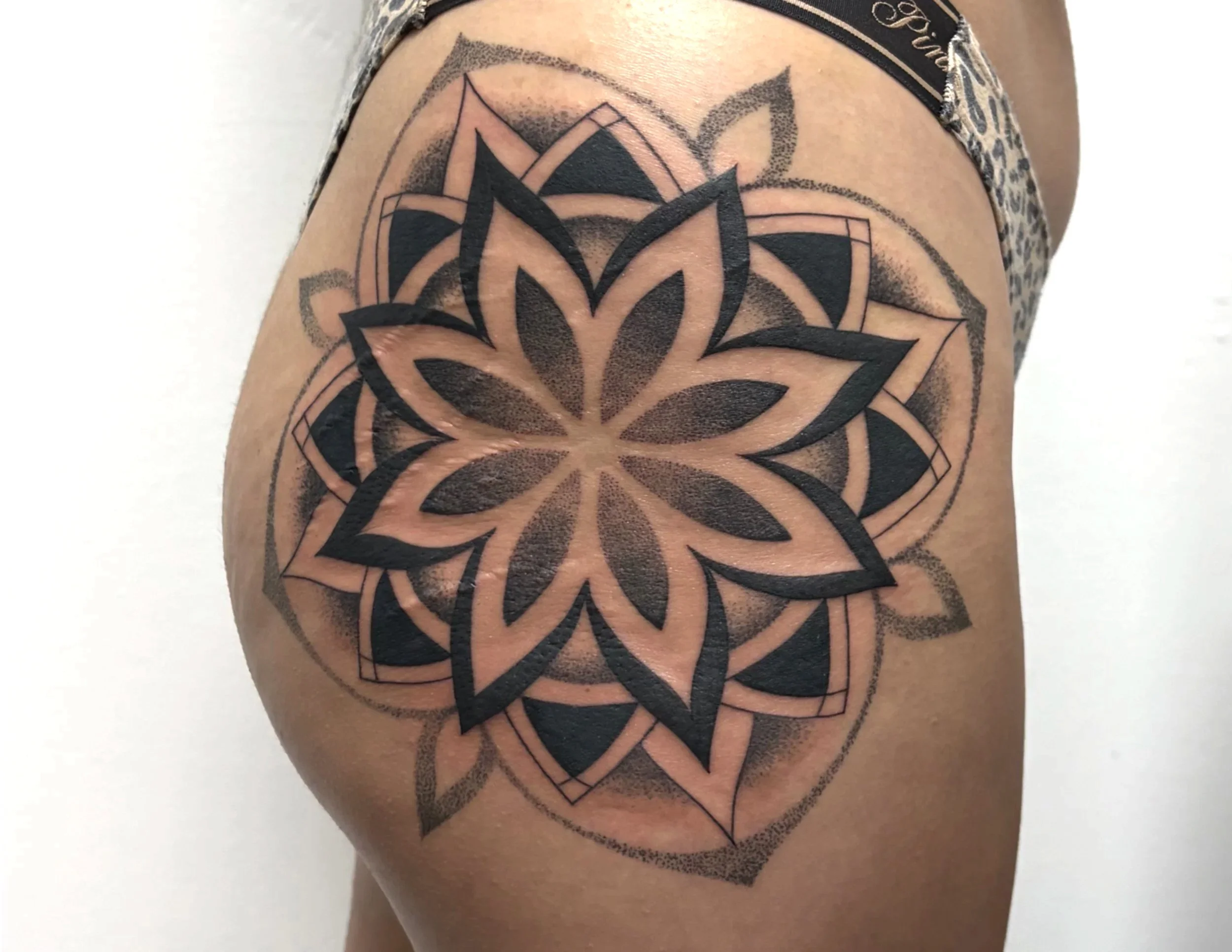 A close-up of a person's upper arm and shoulder with an intricate black tattoo design resembling a geometric floral pattern.