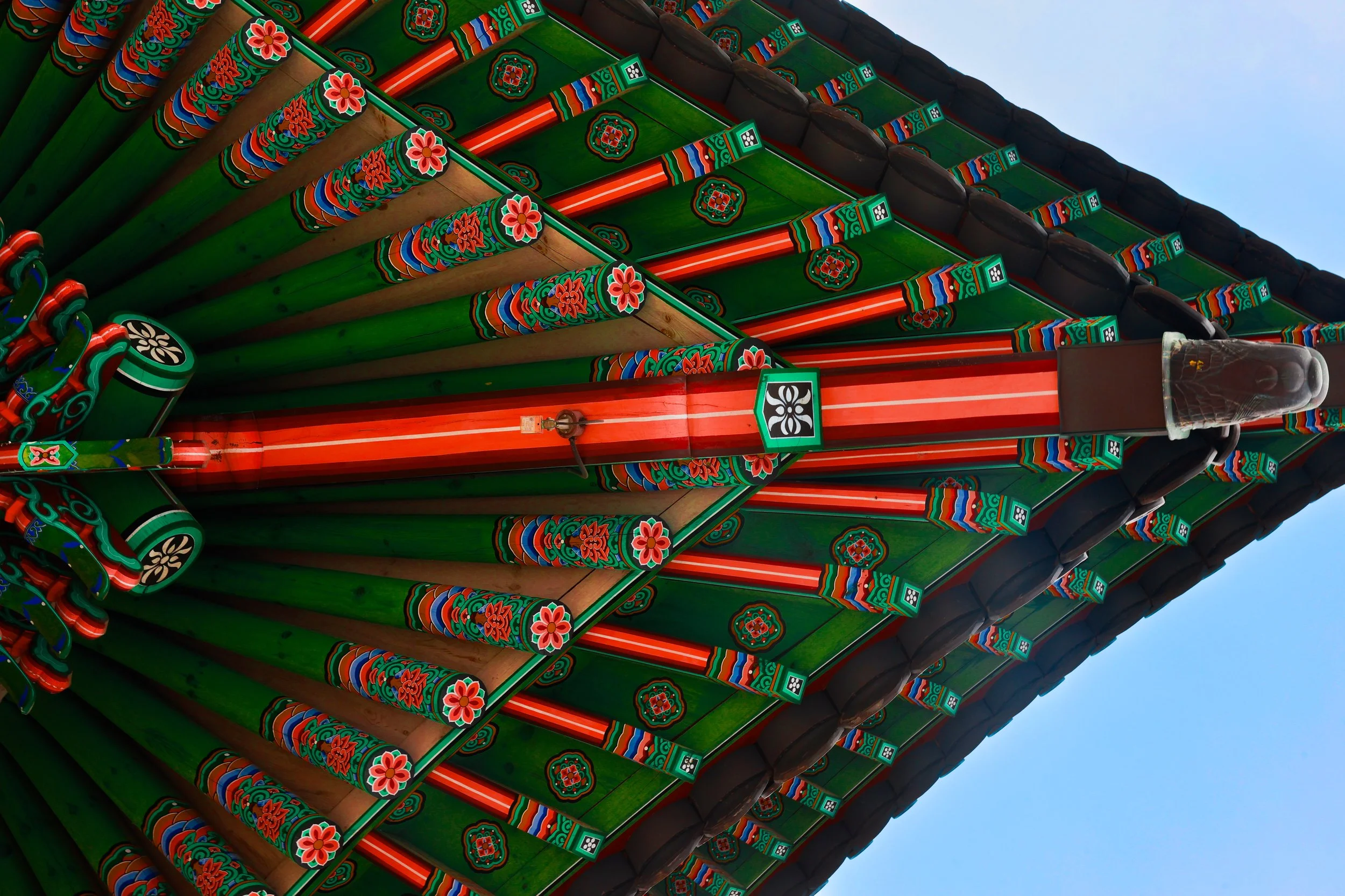 Colorful traditional Korean palace roof with green, red, and black painted patterns and floral details, set against a blue sky.
