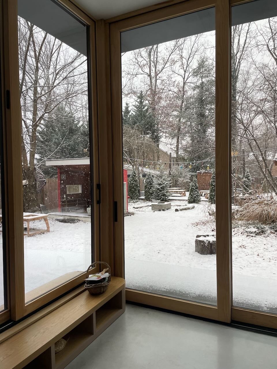 An indoor classroom view looking out through glass walls to the outdoor play yard on a snowy day, highlighting connection between indoor and outdoor learning spaces