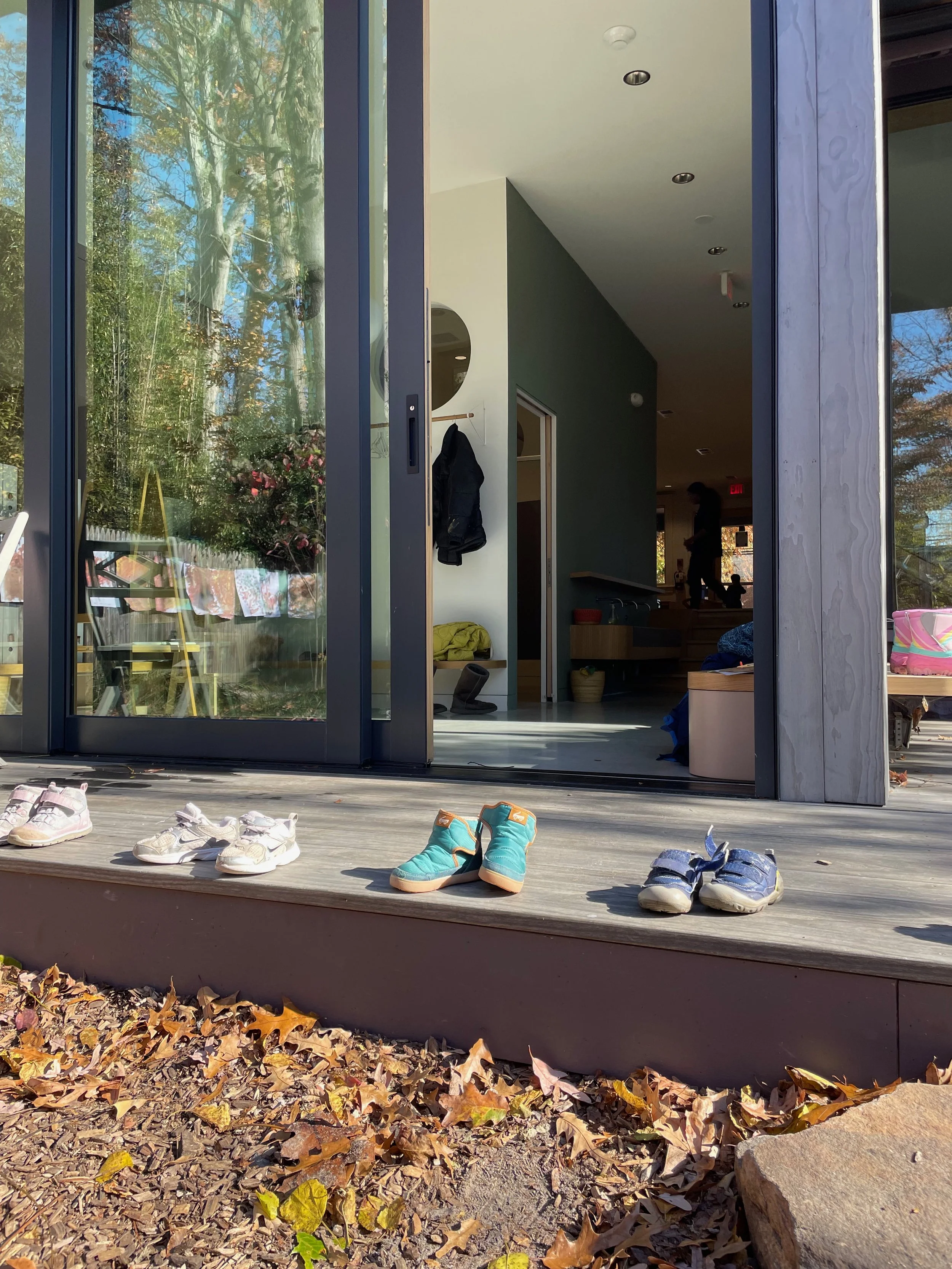 Children's shoes neatly lined up on a sunny deck at Takoma Park Cooperative Nursery School, ready for outdoor play and learning