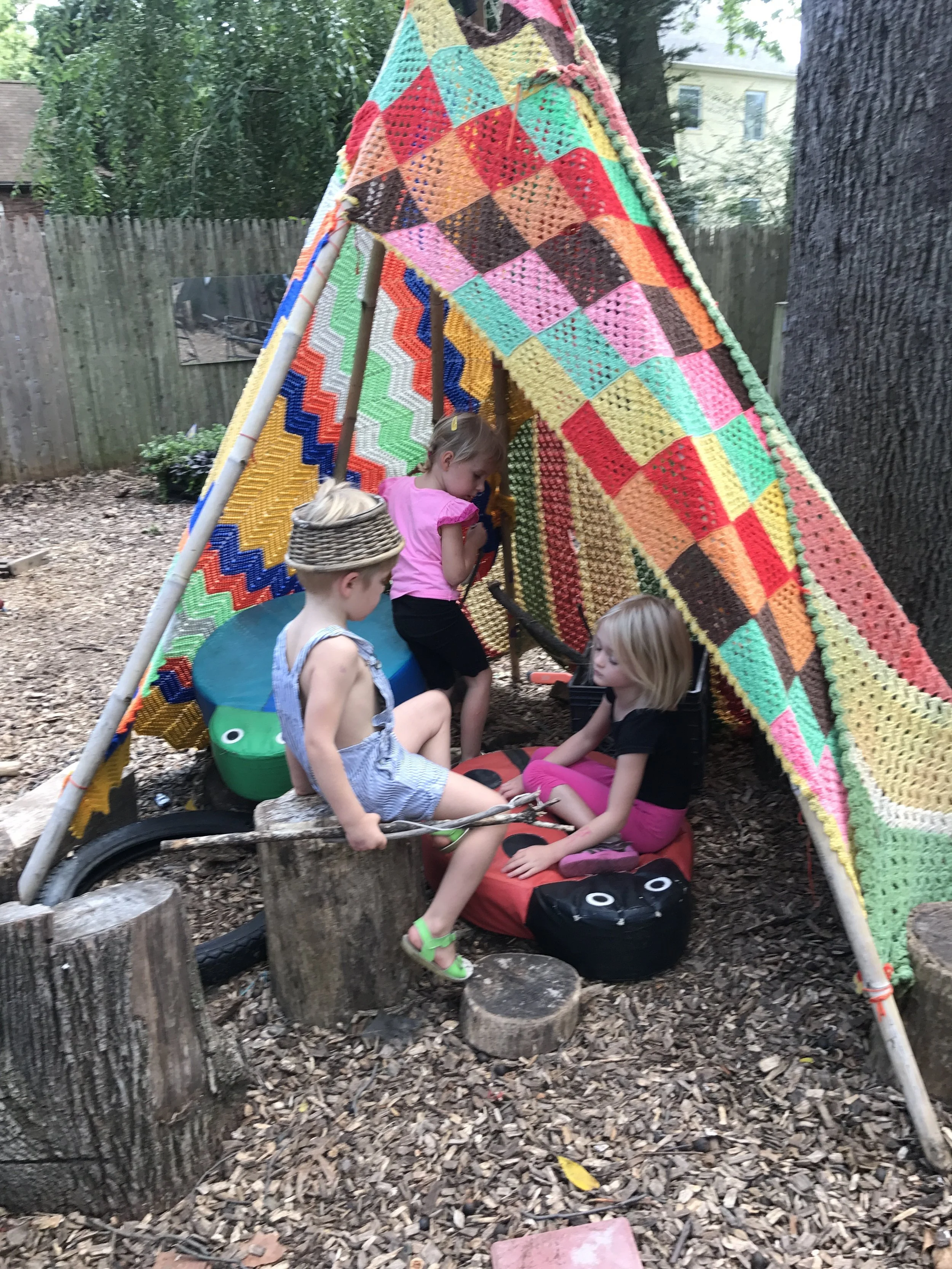 Children engage in outdoor learning through imaginative play, building a cozy blanket fort that supports creativity, community, and connection to nature.