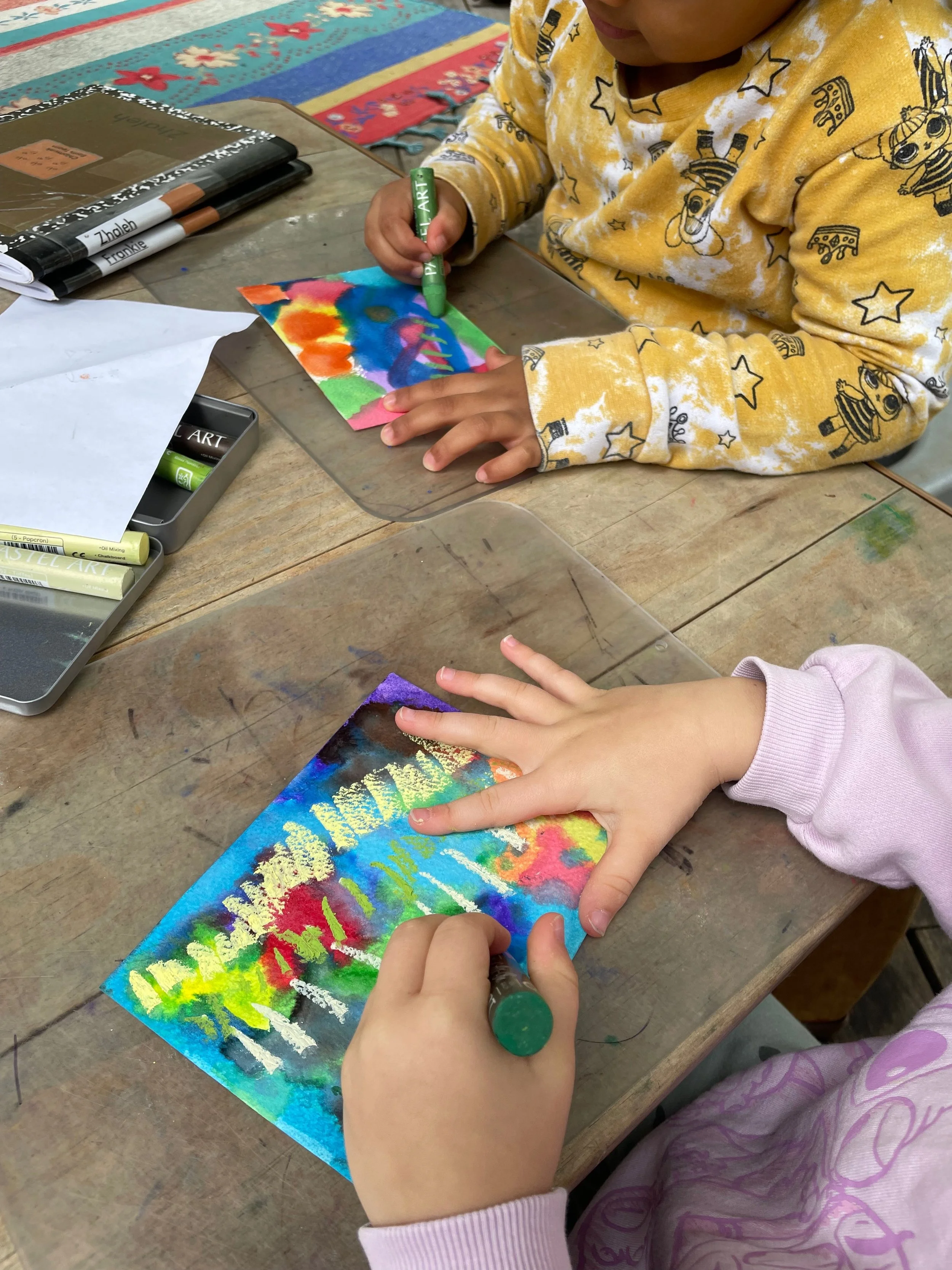 Children creating watercolor and oil pastel artwork in an outdoor classroom at a nature-based preschool