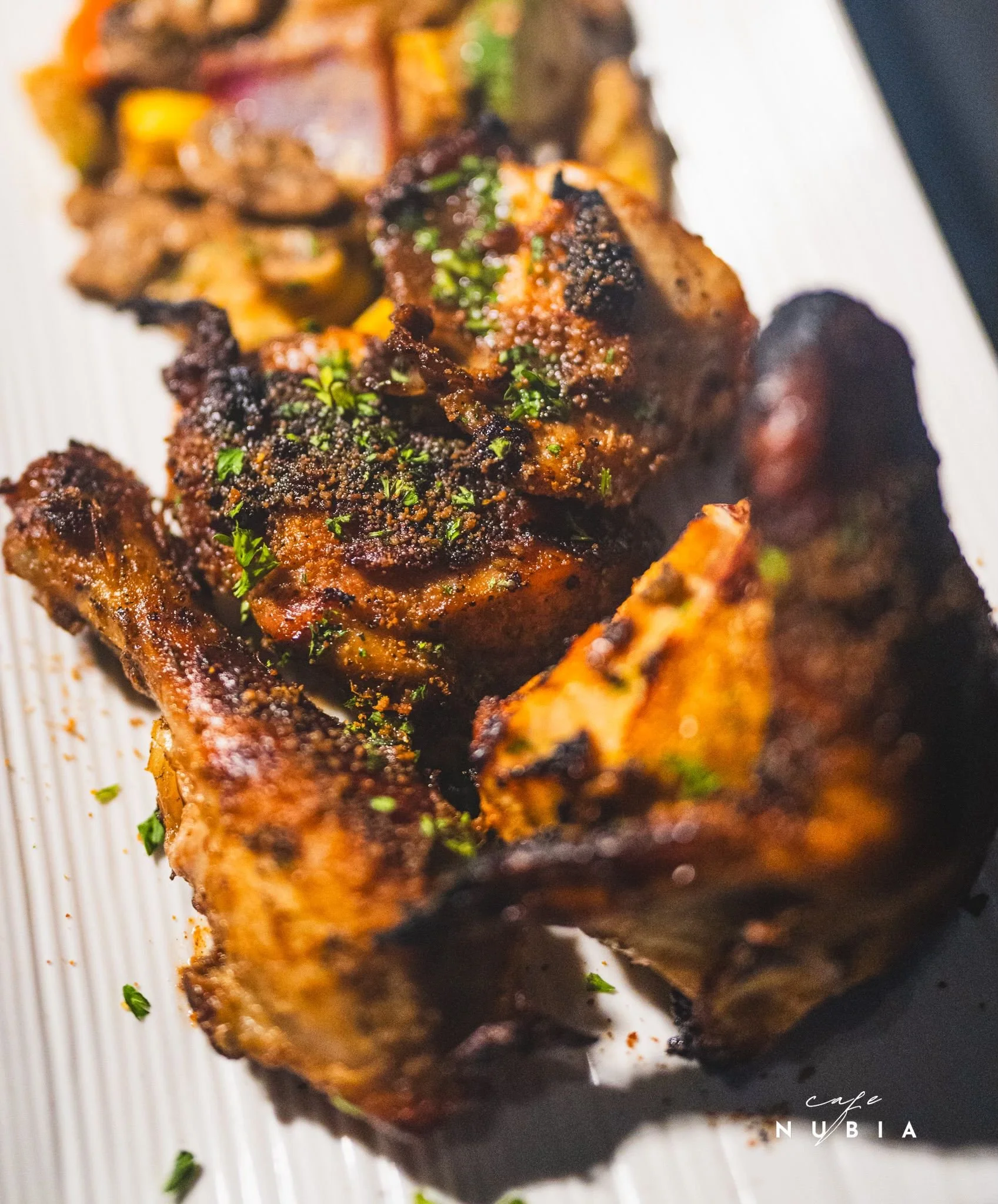 Close-up of a grilled meat or chicken piece garnished with chopped herbs on a white plate, with a blurred dark background.