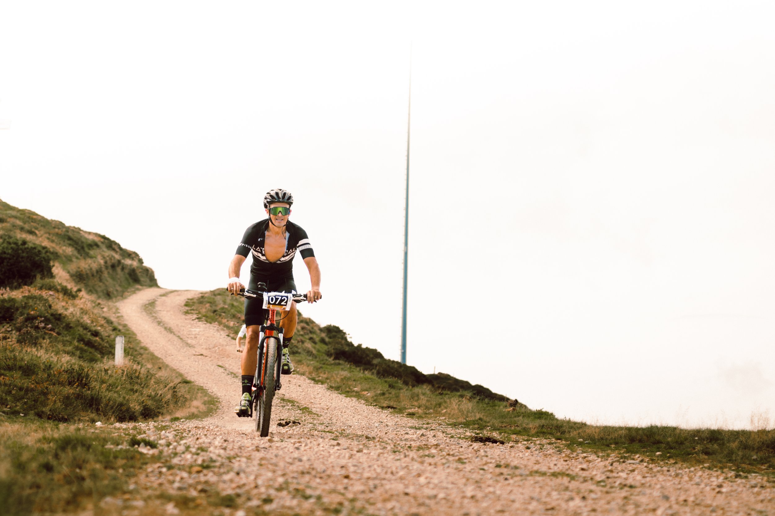 Ciclista con casco y gafas de sol participando en una carrera de ciclismo de montaña en un camino de tierra.