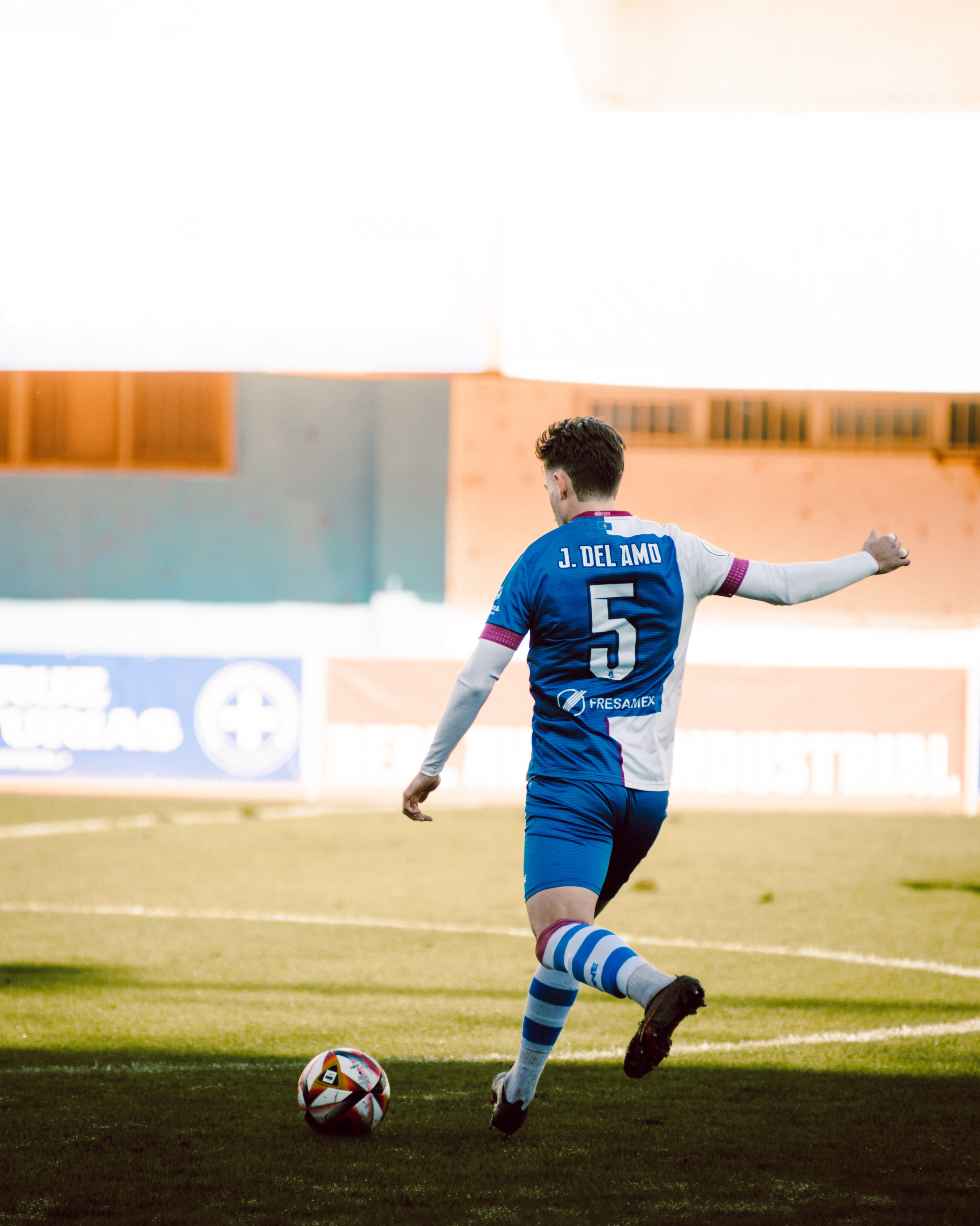 Jugador de fútbol con uniforme azul pateando un balón en el campo.
