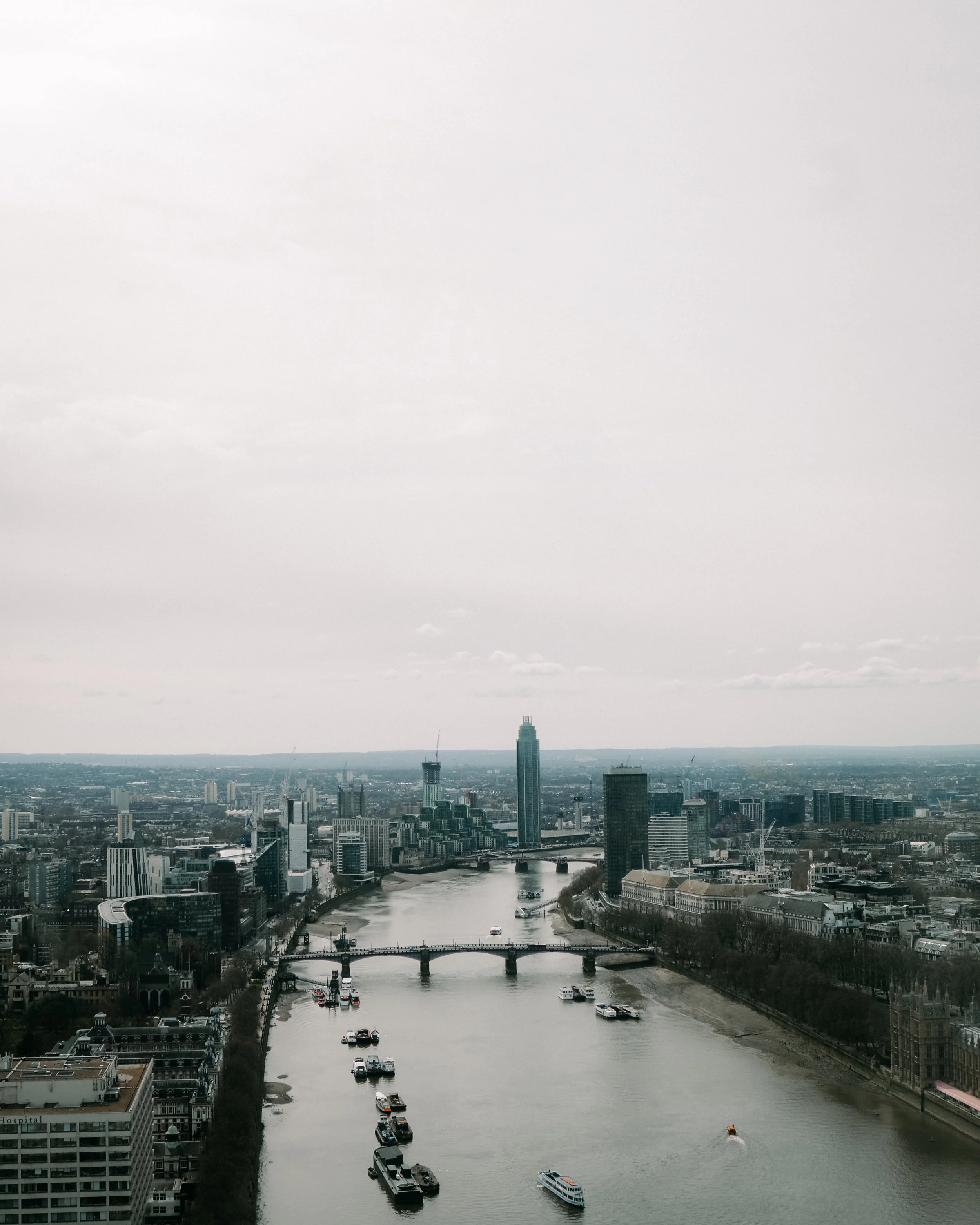 Vista aérea de una ciudad con un río y puentes, rodeada de edificios altos y construcciones modernas. Hay botes navegando en el río.