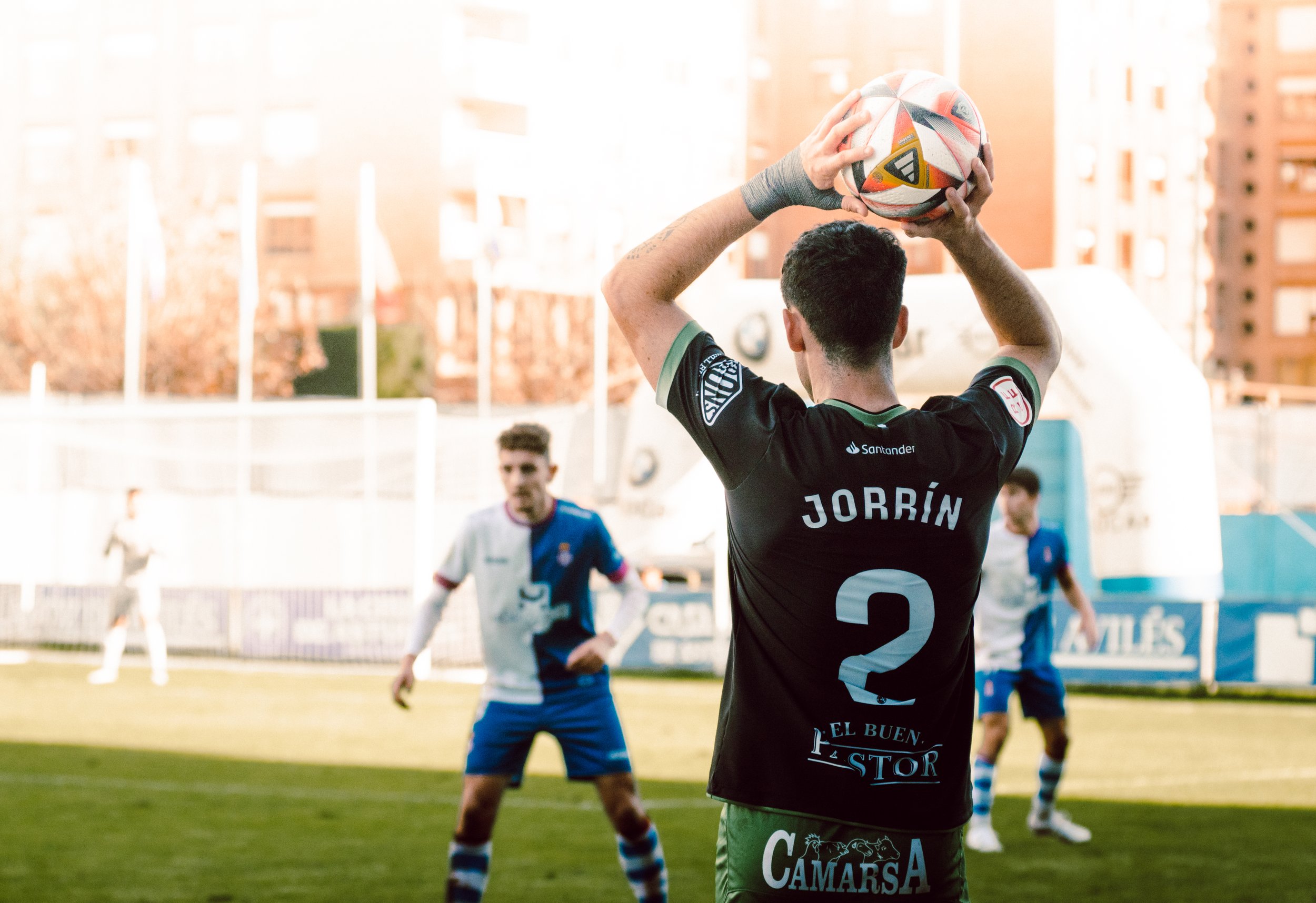 Jugador de fútbol preparando un saque de banda durante un partido, con otro jugador al frente defendiendo.