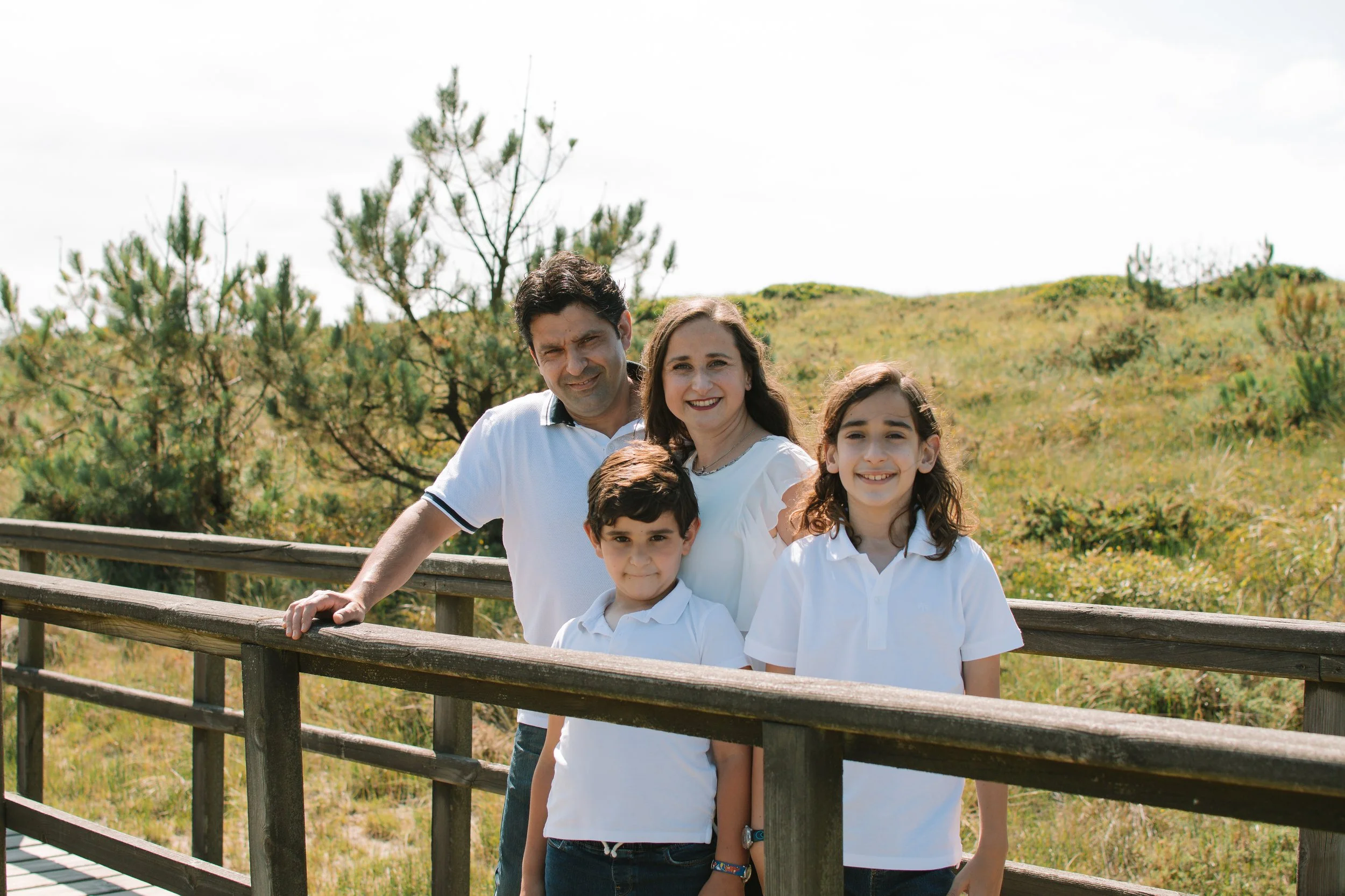 Una familia de cuatro personas, dos adultos y dos niños, posando en un puente de madera al aire libre con vegetación de fondo.
