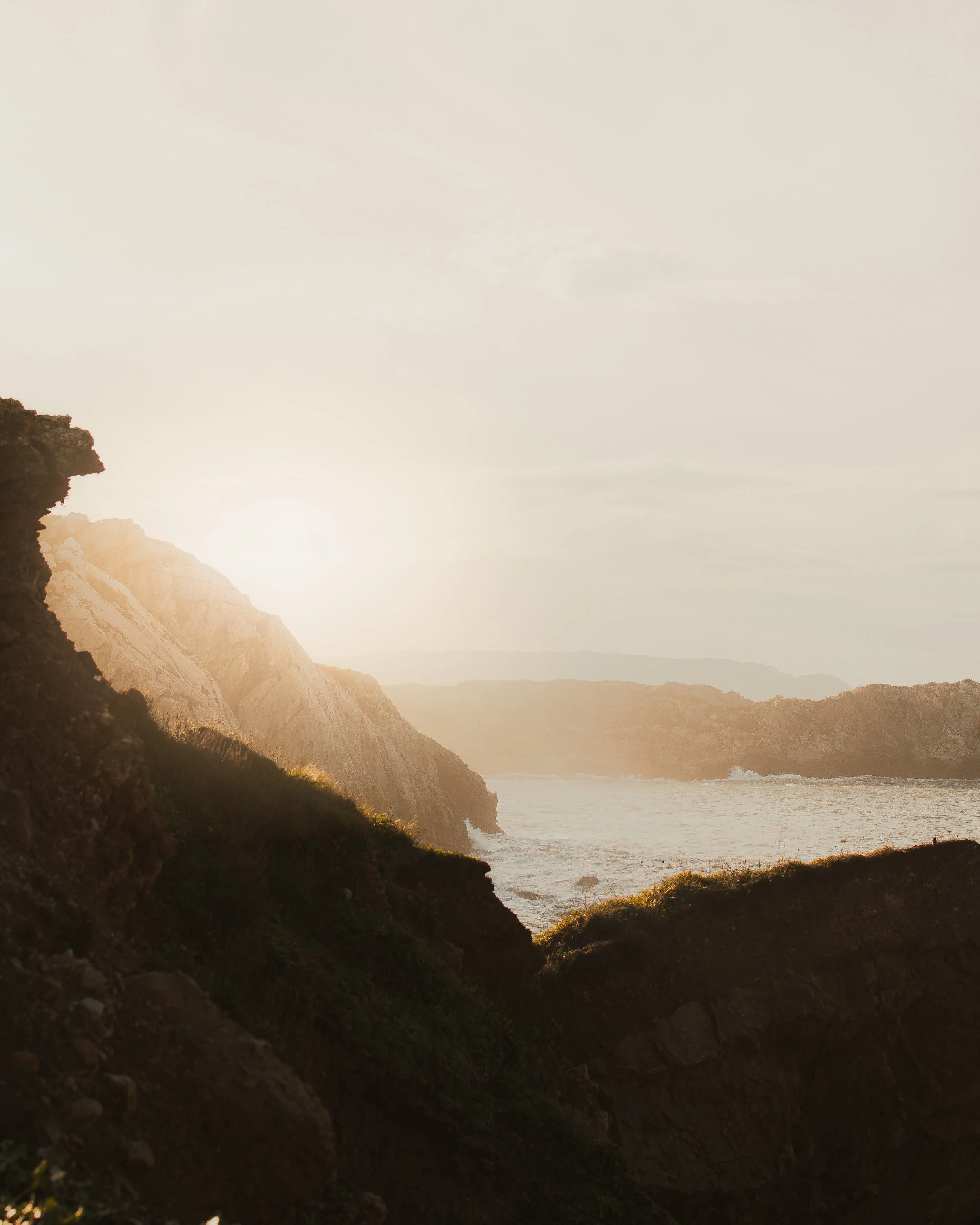 Paisaje costero en Asturias con acantilados, el sol al atardecer y el mar en el horizonte.