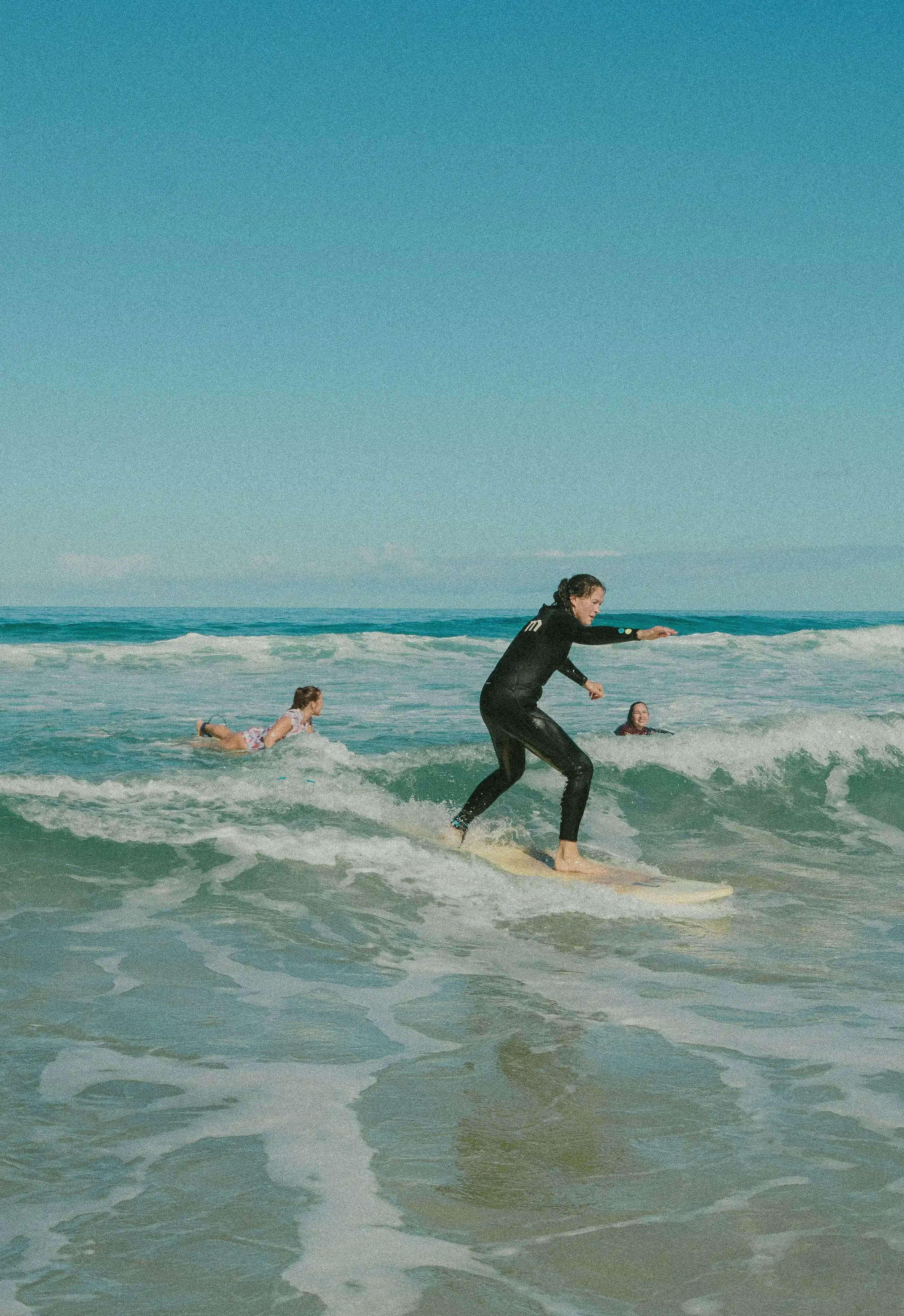 Žena šťastně surfuje na vlnách během jóga retreatu na Fuerteventura. Kombinace jógy, surfování a aktivního odpočinku pro radost z pohybu.