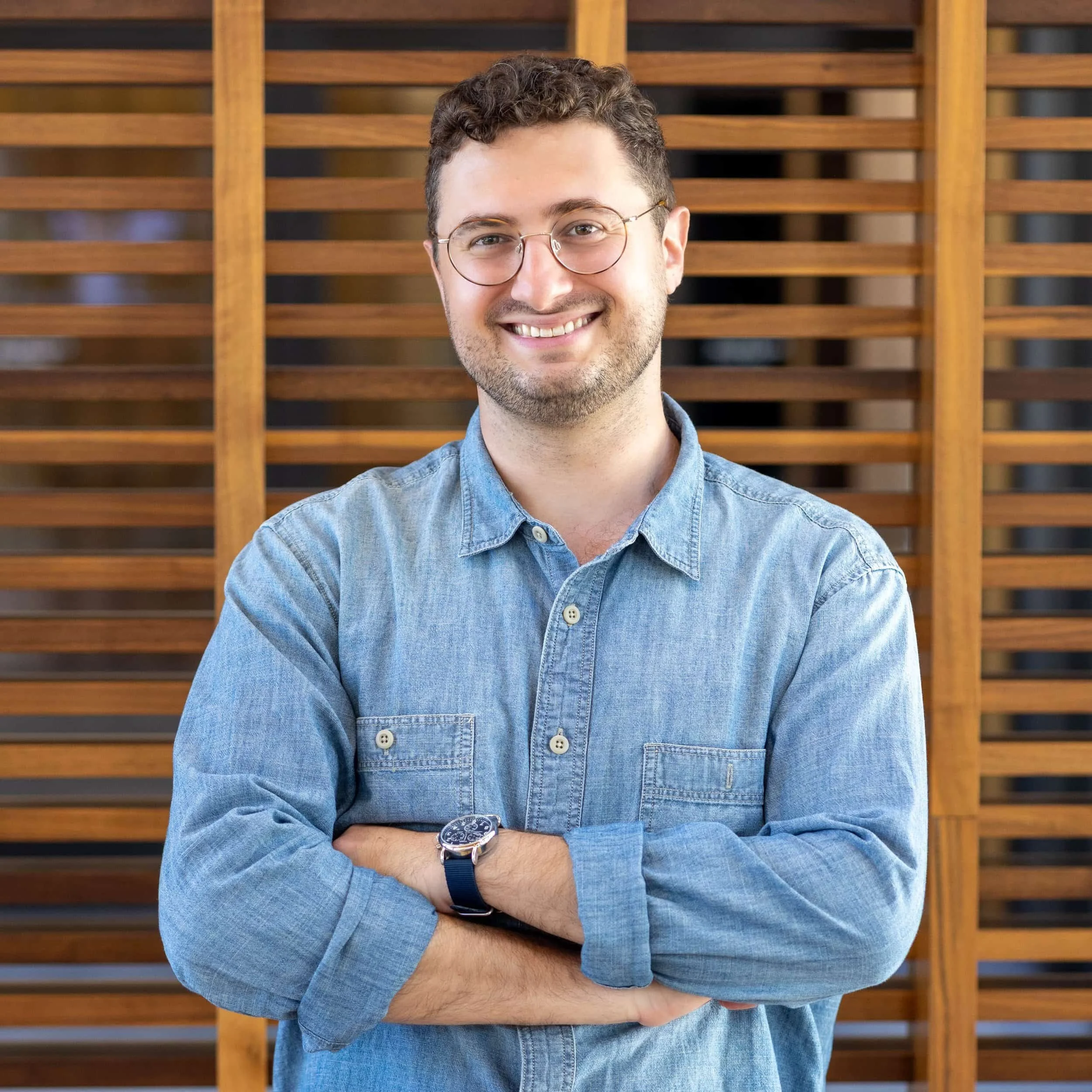 Smiling Therapist with glasses in denim shirt stands with arms crossed, embodying confidence inspired by Self Worth therapy.