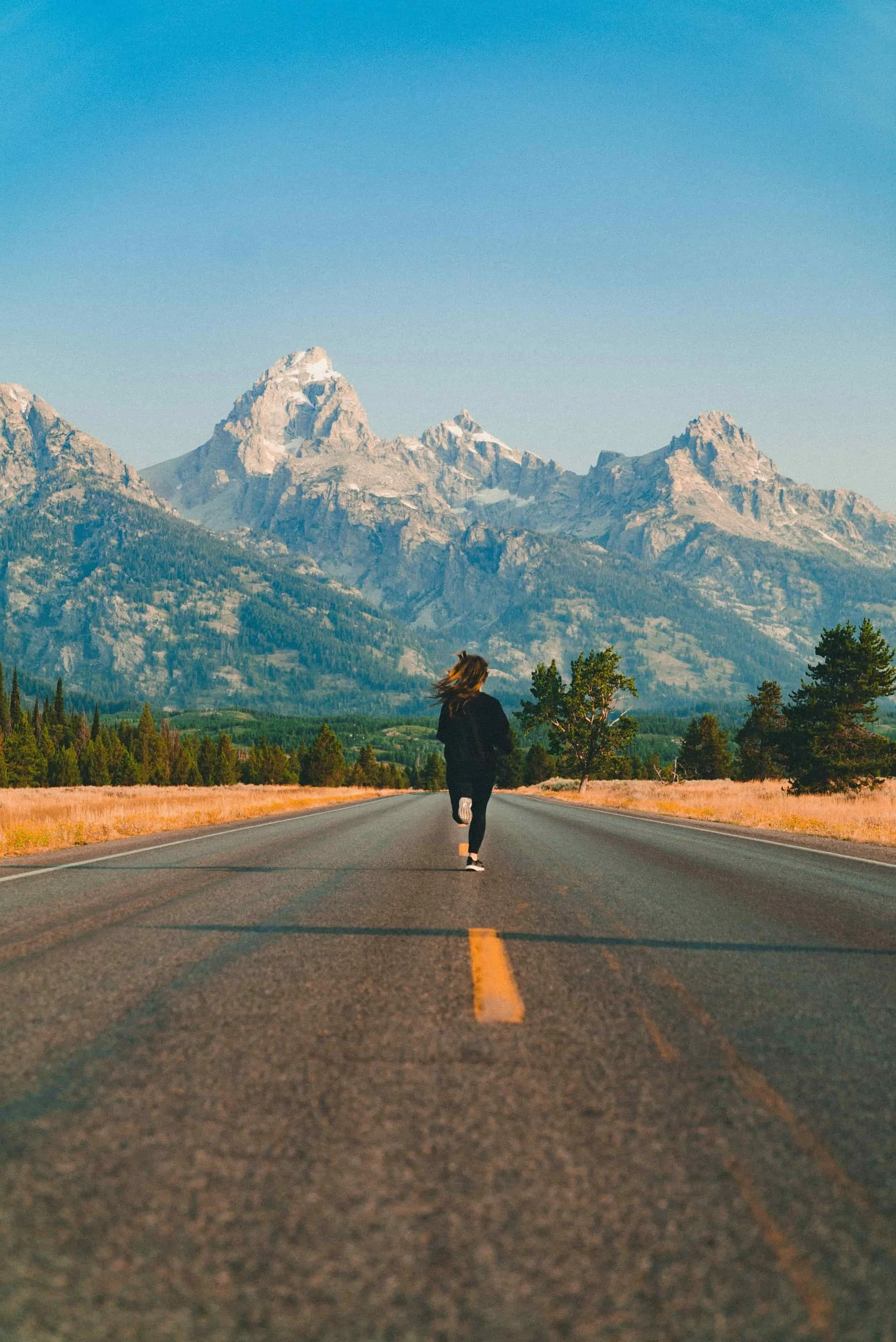 Person running down an empty road toward mountains, embracing self worth therapy under a clear blue sky and trees on either side.