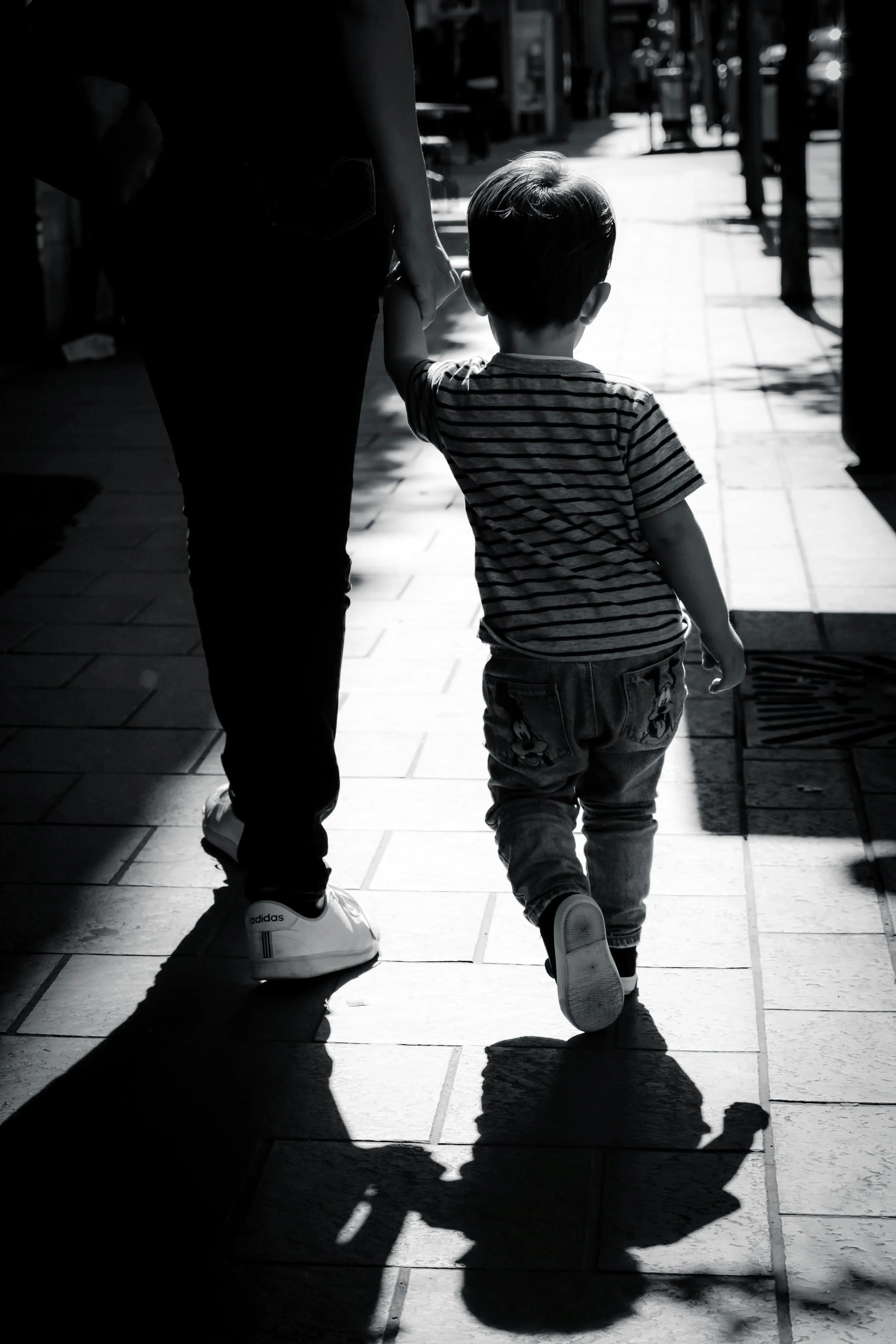A child and adult, hand in hand, walk a sunlit sidewalk—an everyday moment reflecting the bond nurtured by attachment therapy.