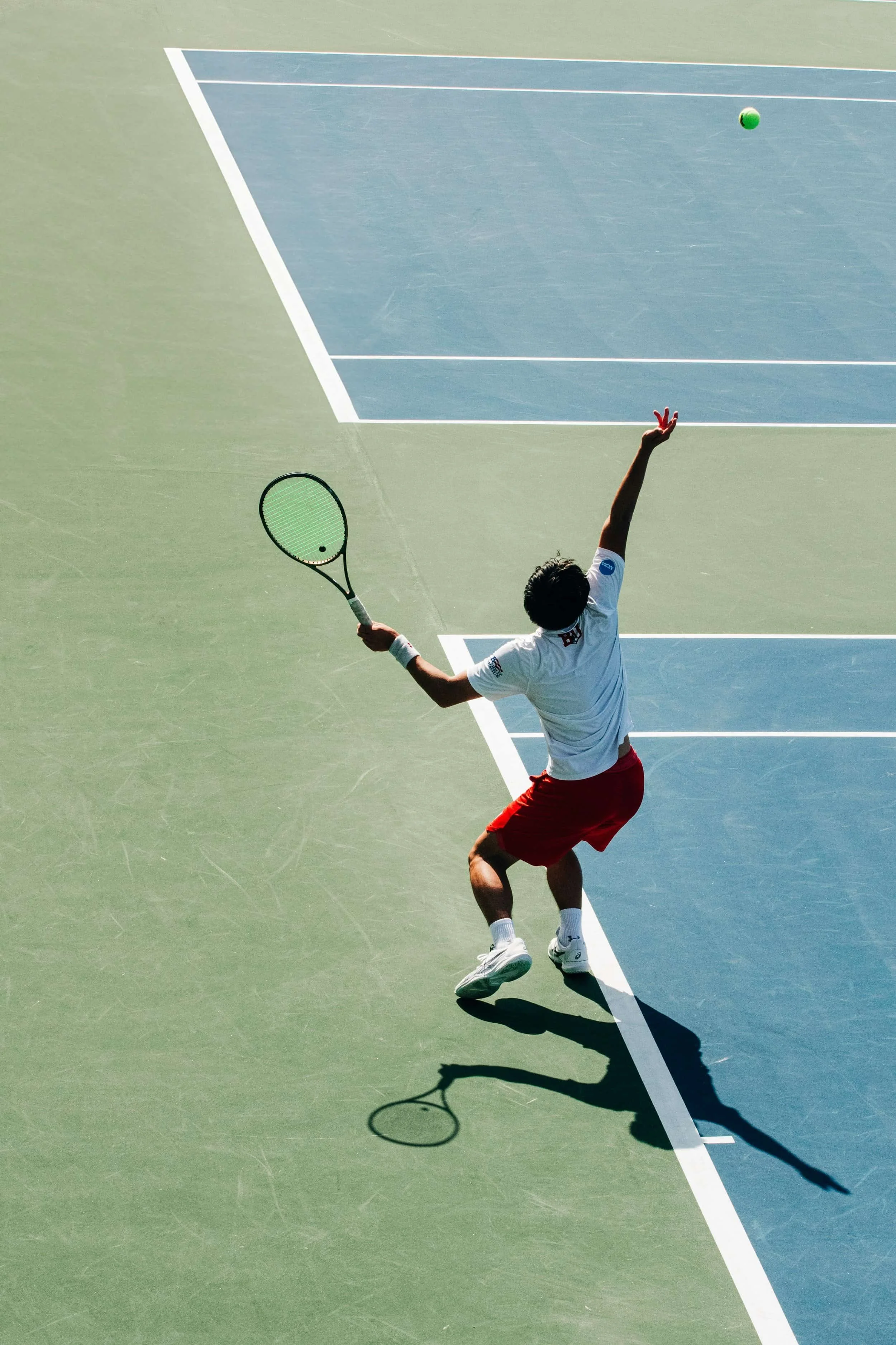 Tennis player in red shorts serves mid-jump on outdoor court, showing confidence and self worth therapy in action.
