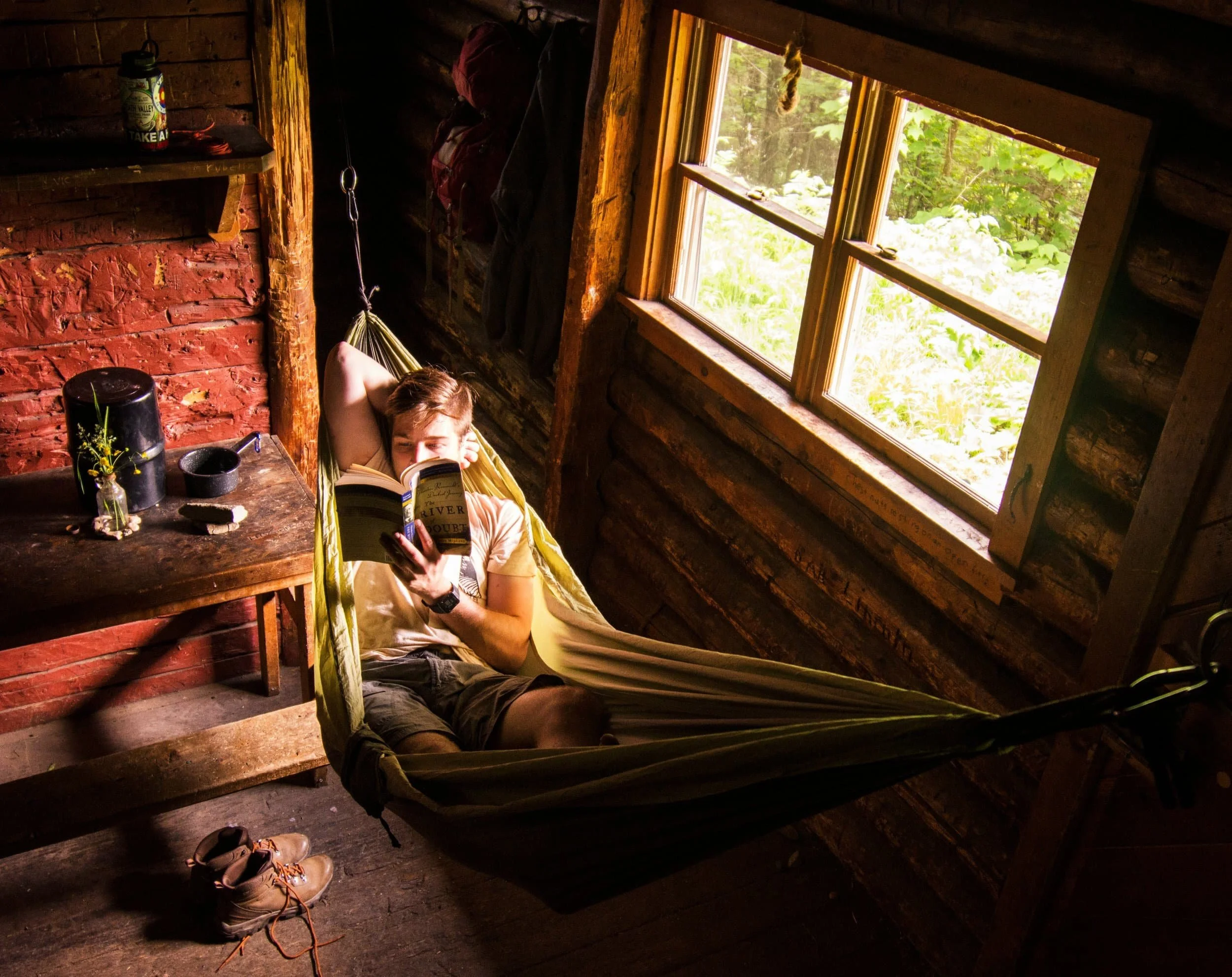 Person relaxing in a hammock inside a rustic cabin, reading about psychodynamic therapy as sunlight streams through the window.